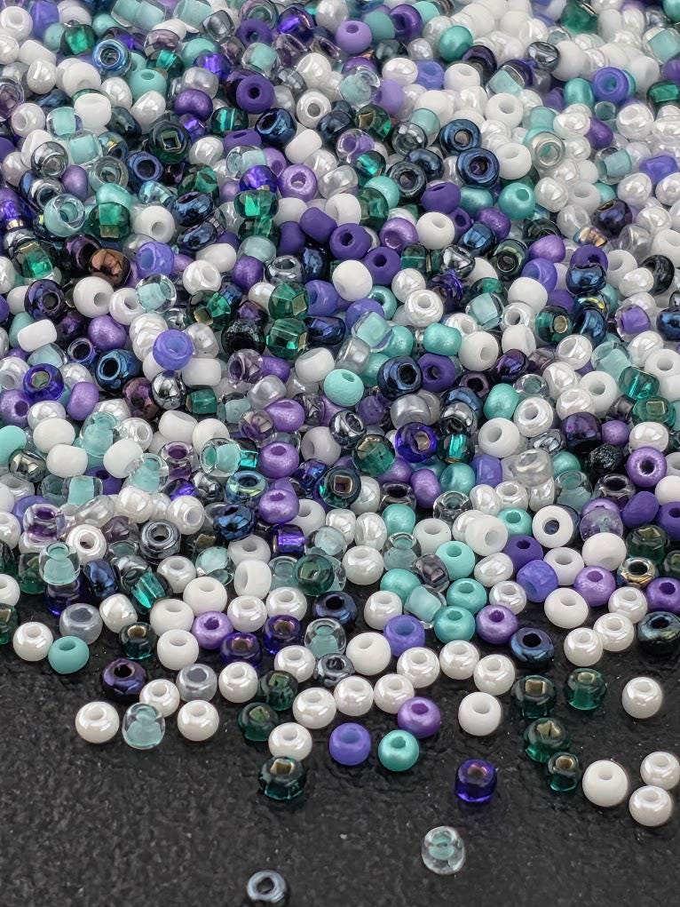 A colorful pile of multicolored beads, including white, purple, blue, and green, scattered on a dark surface.