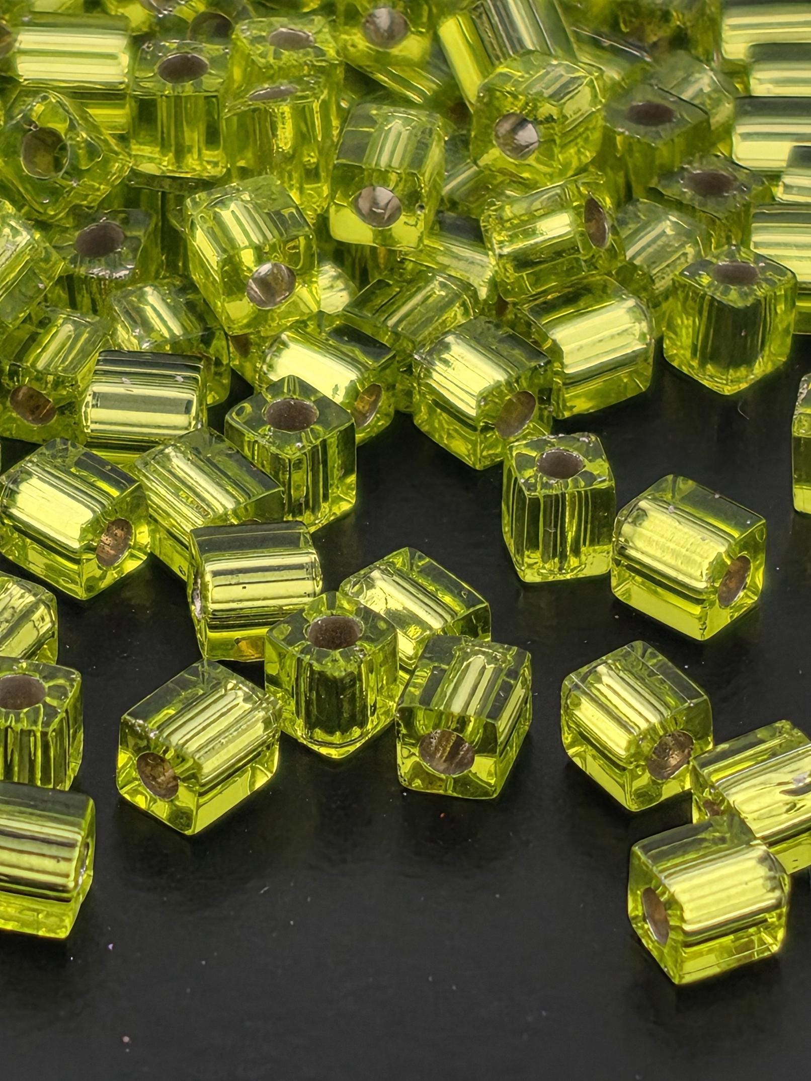 a collection of small, clear, and shiny green glass beads scattered on a dark background.