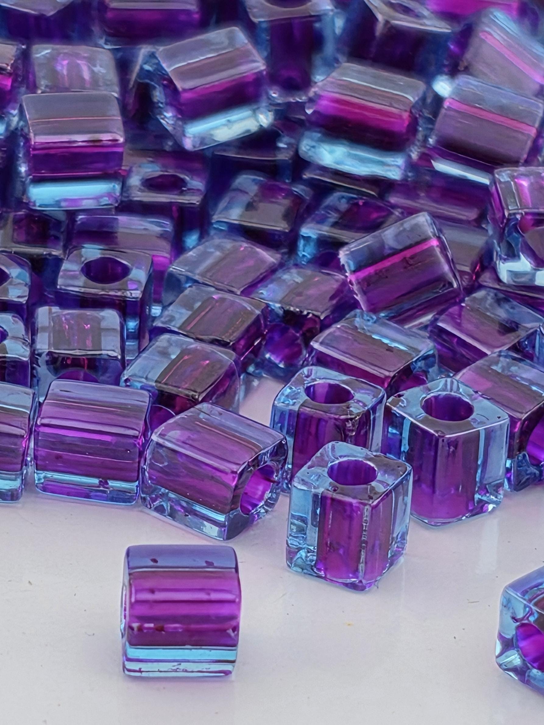 numerous small, clear, and square-shaped purple and blue glass beads scattered across a surface.