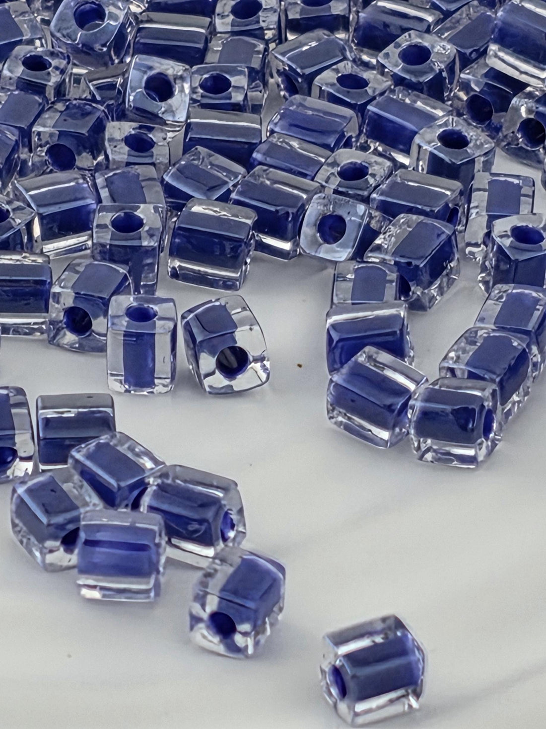 a collection of clear glass beads in various shades of blue, scattered across a white surface.