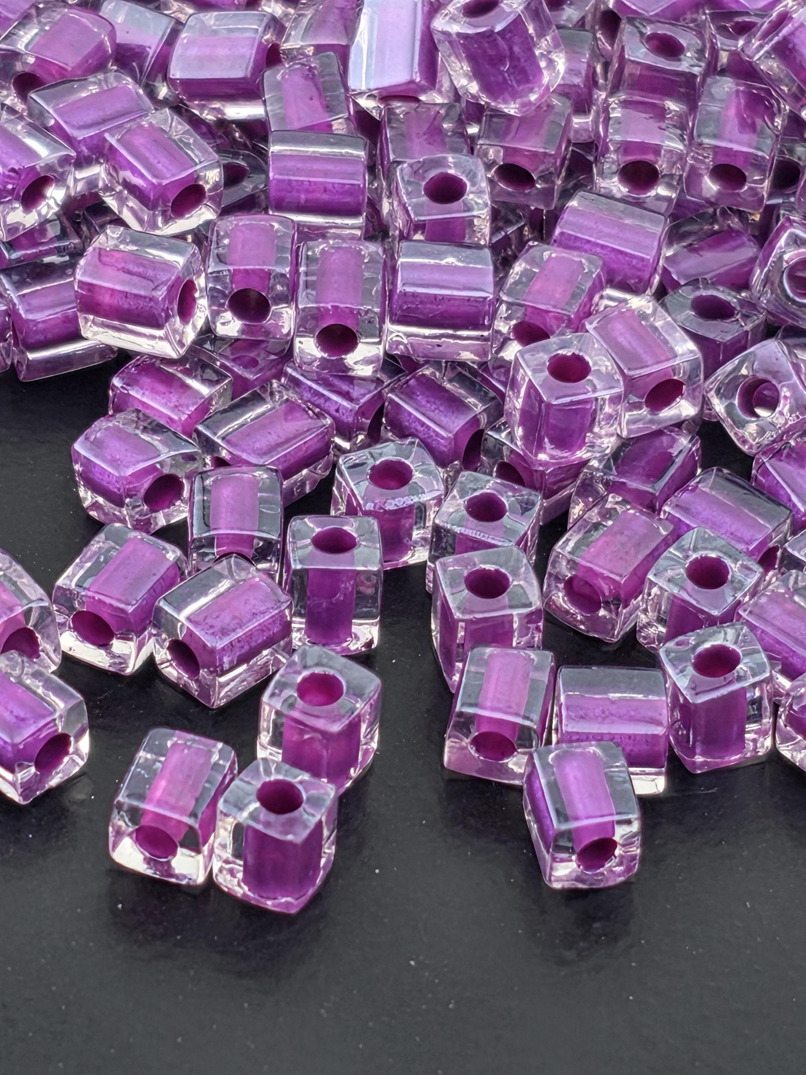 a close-up view of numerous clear glass beads in shades of purple, scattered on a dark background.