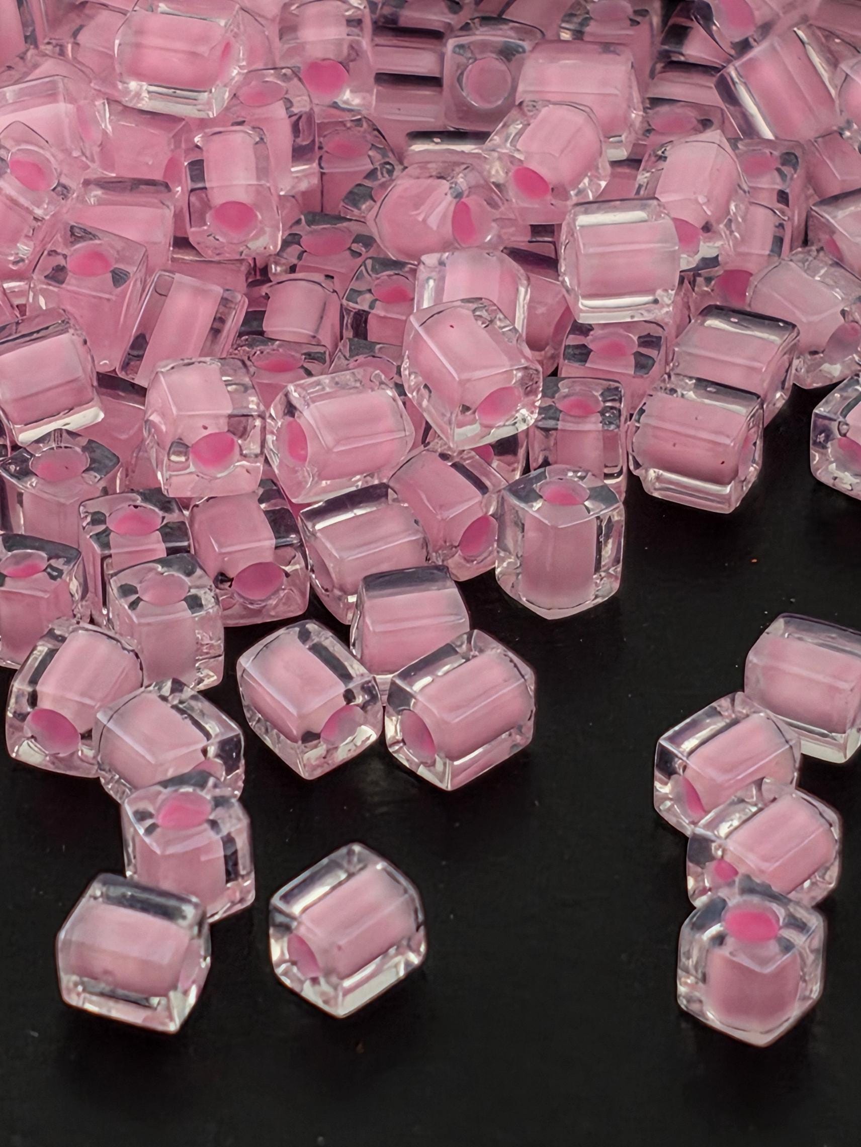 a close-up view of numerous clear, transparent, and pink-colored cubes or beads scattered on a dark background.