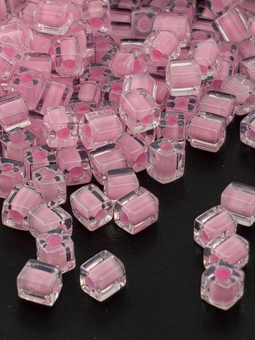 a close-up view of numerous clear, transparent, and pink-colored cubes or beads scattered on a dark background.