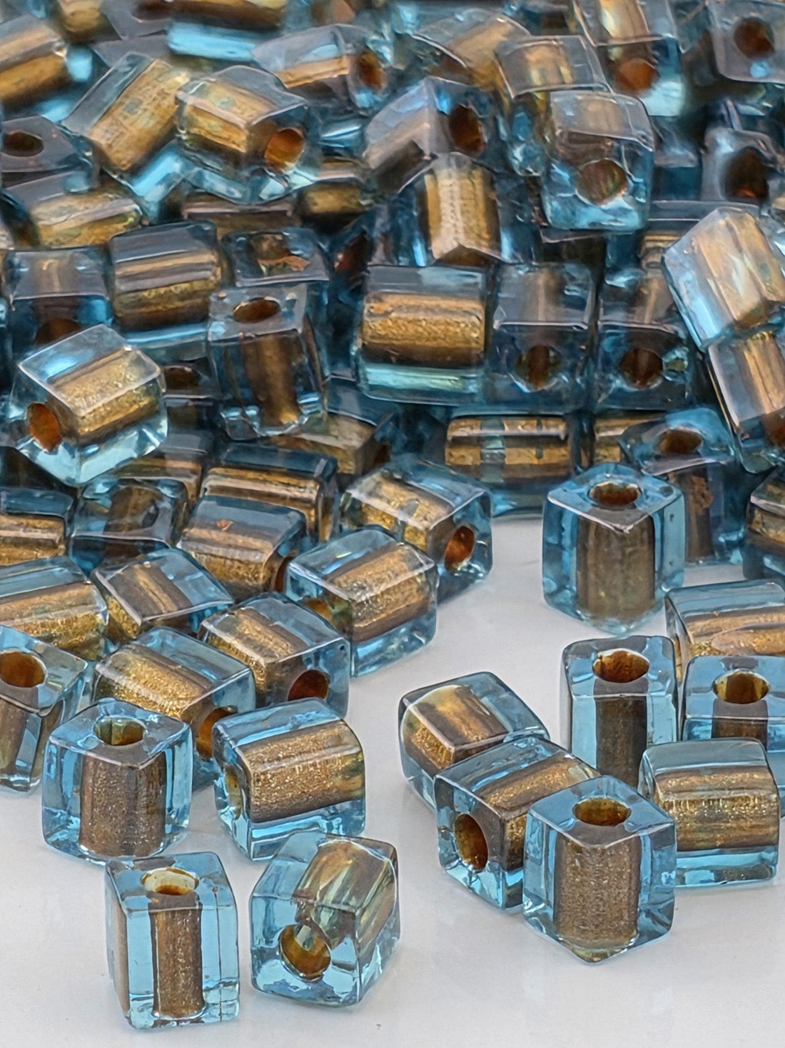 The image is a close-up of numerous small, clear glass beads in various shades of blue and gold, scattered across a surface.