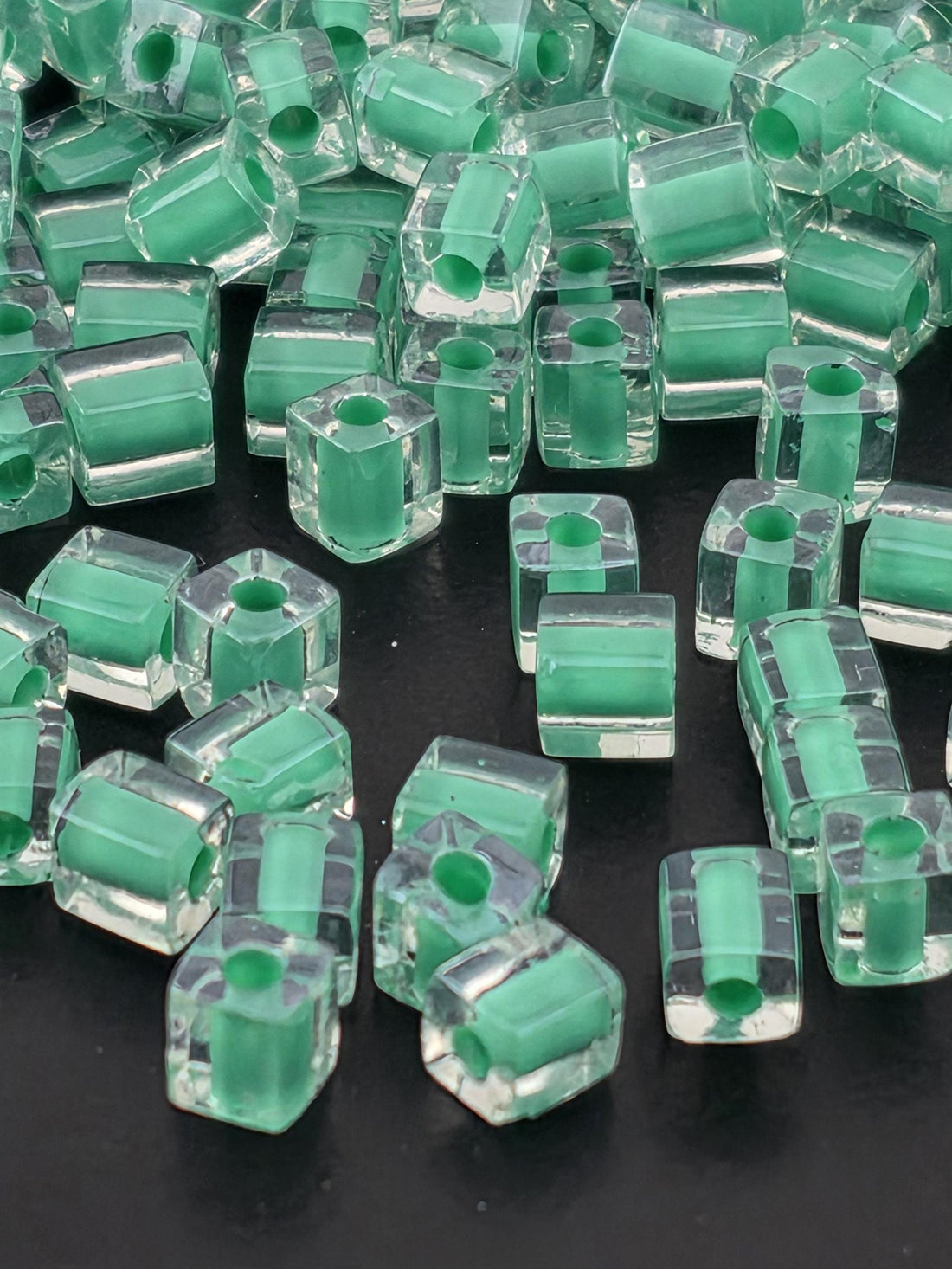 a collection of clear glass beads in various shades of green, scattered on a dark background.