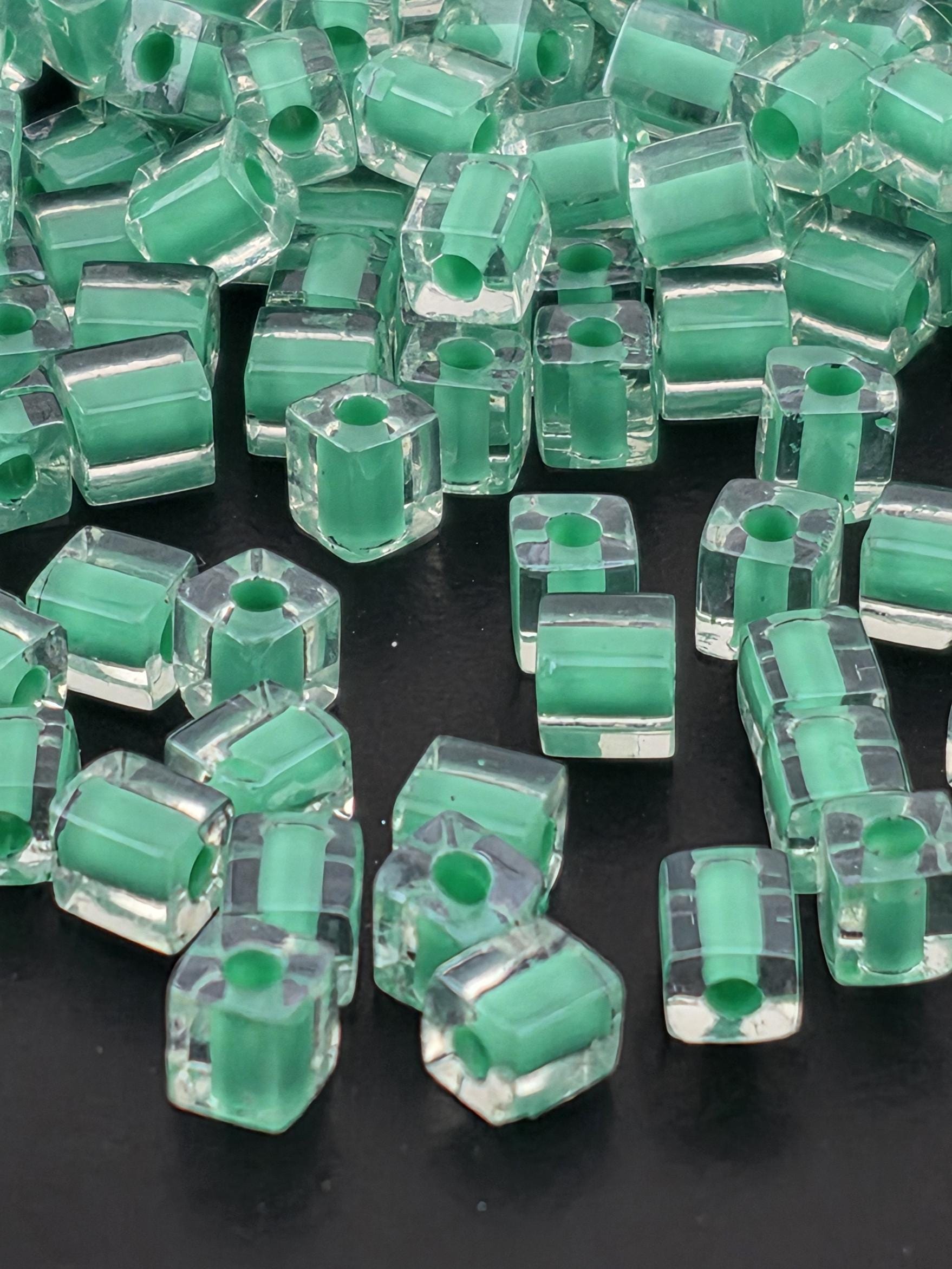 a collection of clear glass beads in various shades of green, scattered on a dark background.