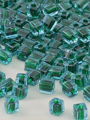 The image is a close-up of numerous small, clear glass beads in various shades of green, scattered across a surface.