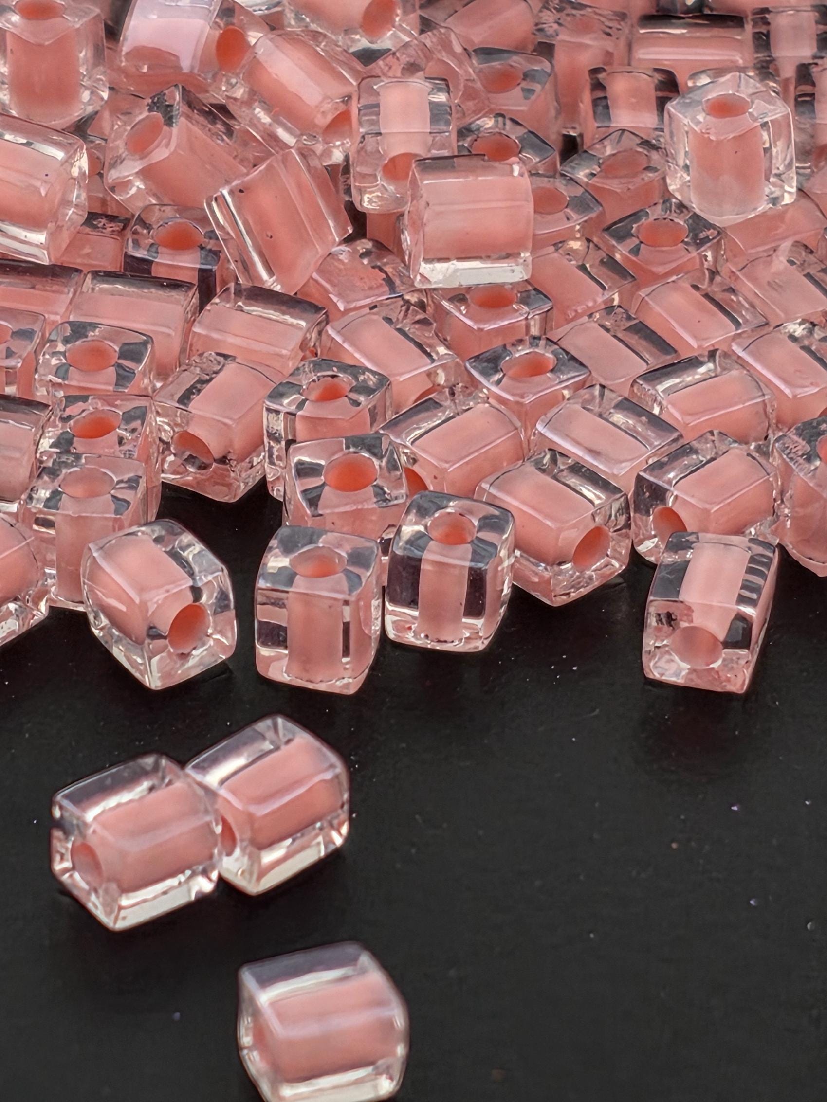 a close-up view of numerous clear, pink-colored glass beads scattered on a dark background.