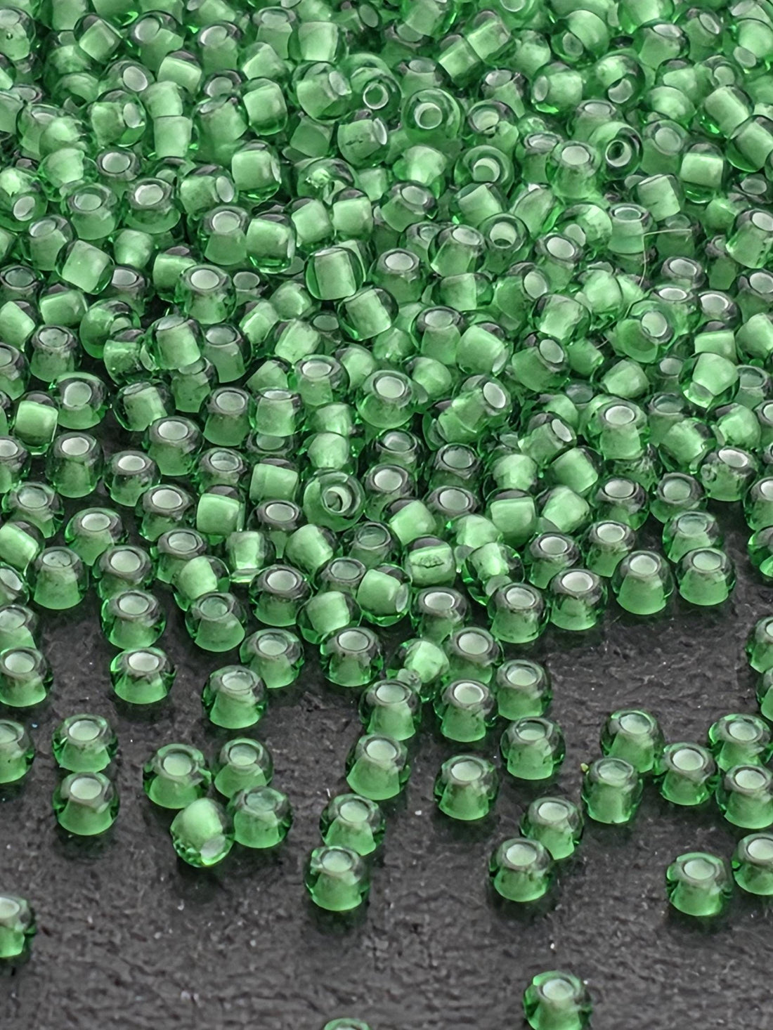 a close-up view of numerous green glass beads scattered on a dark surface.