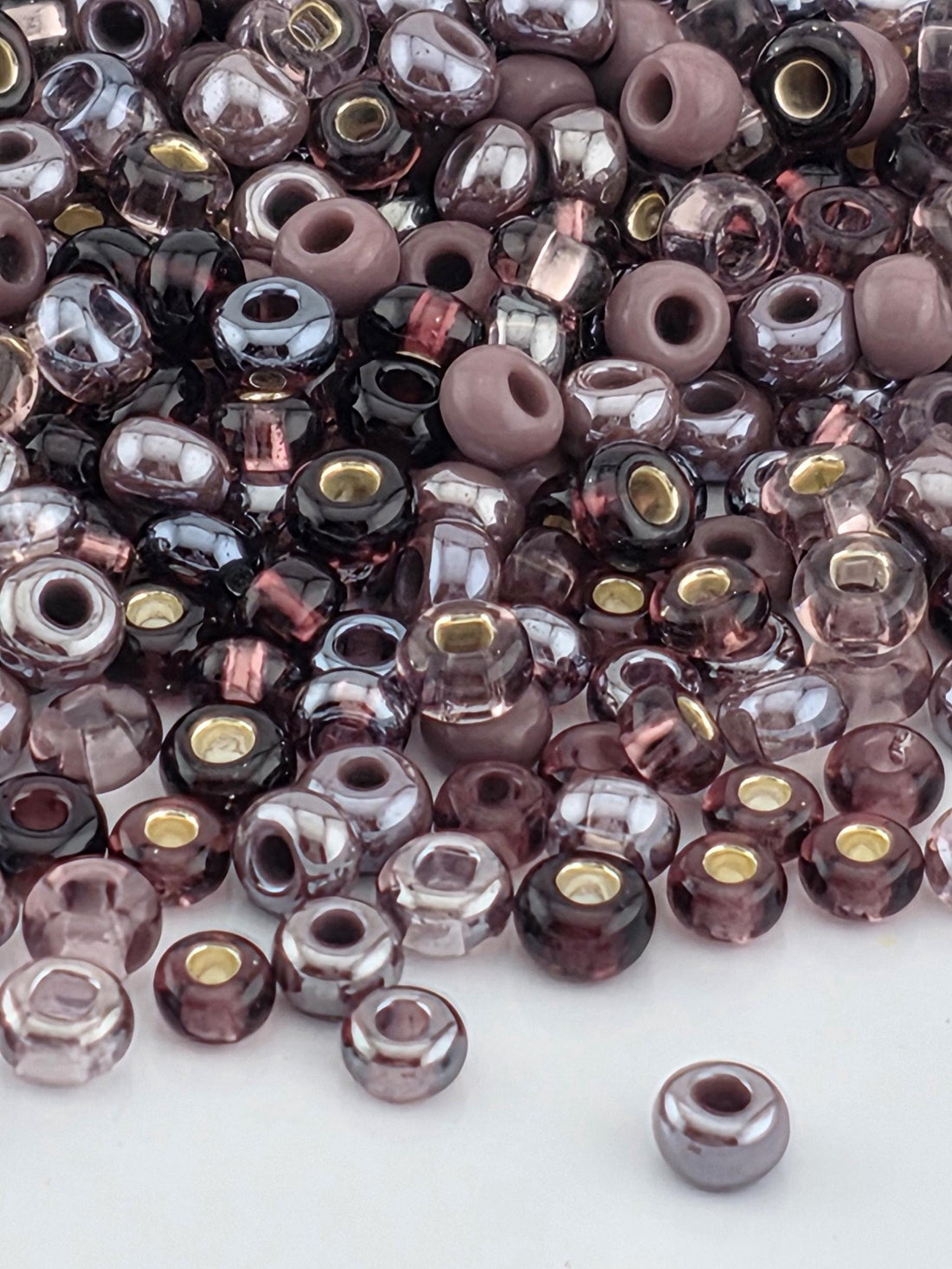 a large pile of various colored glass beads, including shades of purple, pink, and gray, scattered across a surface.