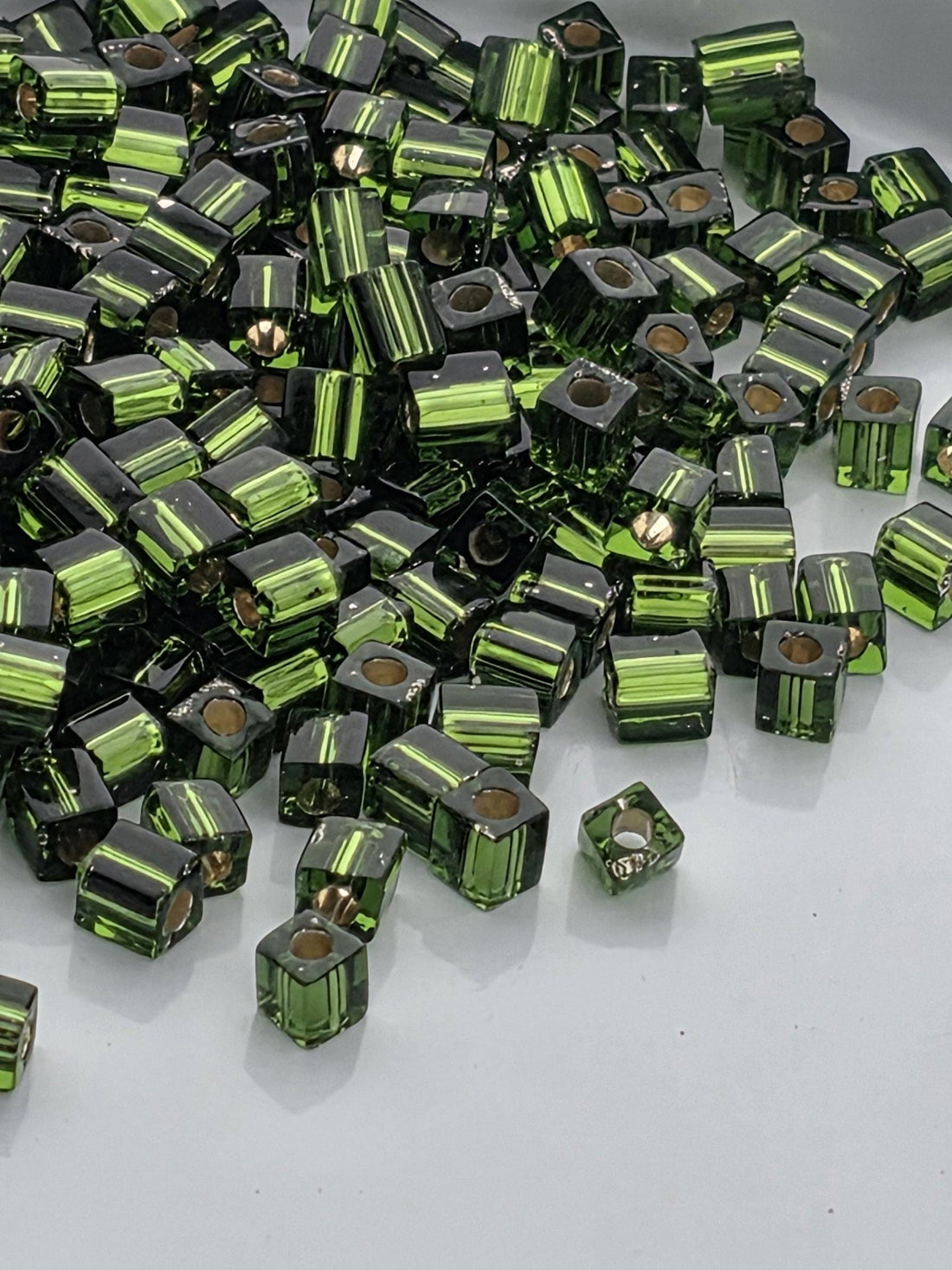 a pile of green and black glass beads or cubes, scattered on a white surface.