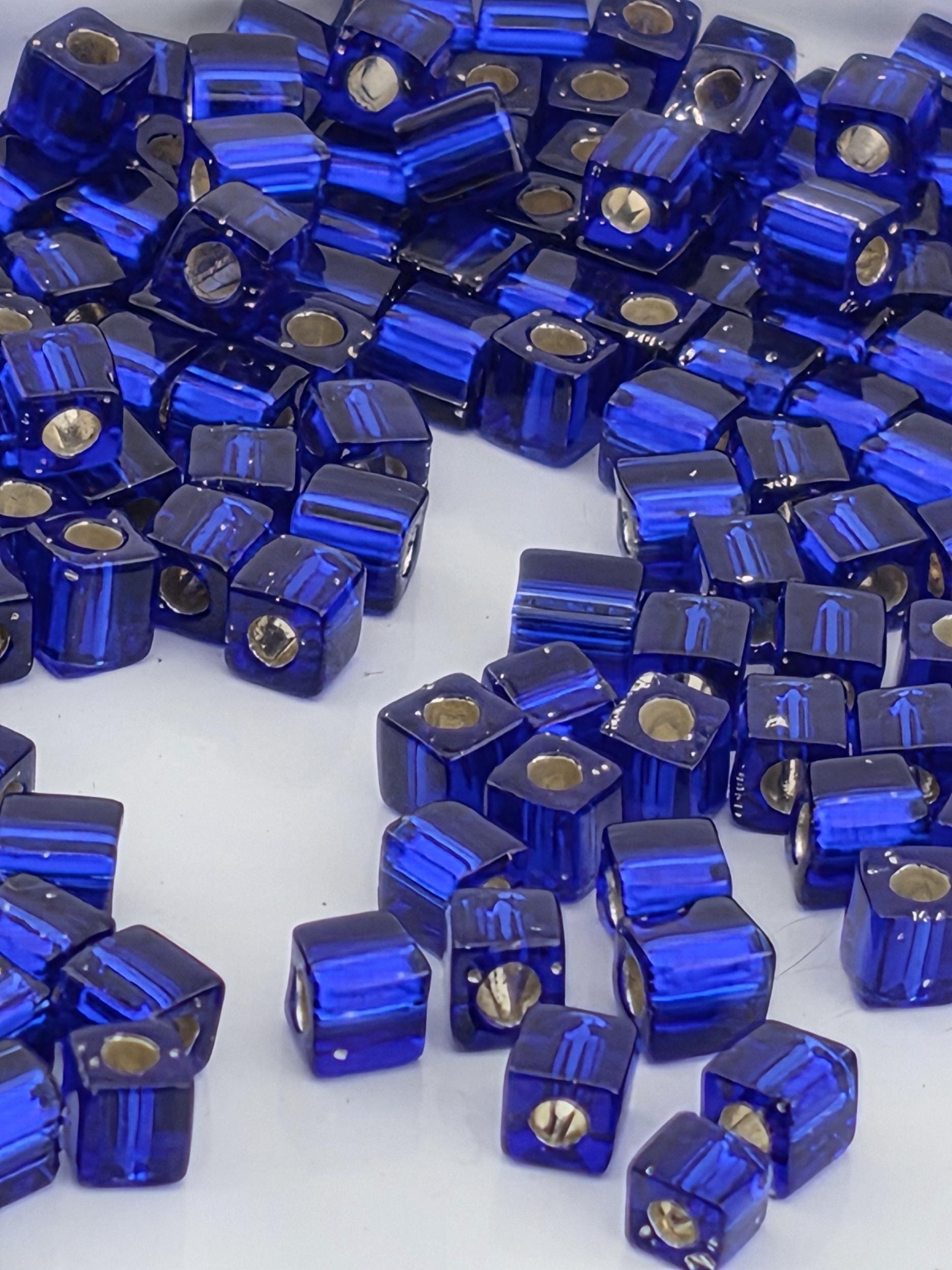 a collection of blue glass beads or cubes arranged in a scattered pattern on a white background.