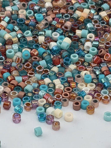 A colorful pile of multicolored beads, including various shades of blue, green, brown, and orange, scattered across a surface.