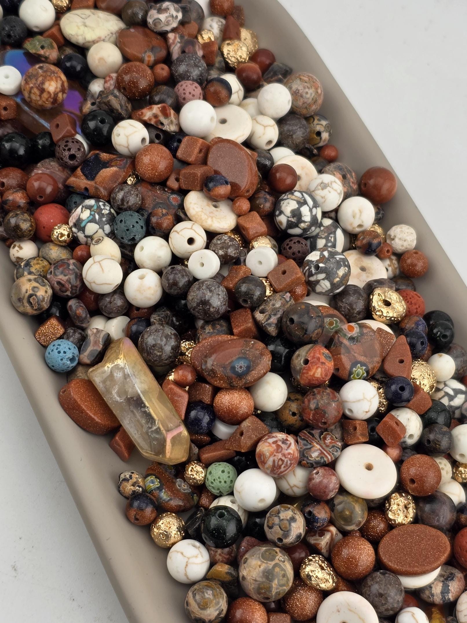 A collection of various beads, gemstones, and crystals of different shapes, sizes, and colors, including white, brown, black, and multicolored stones, arranged in a visually appealing manner.