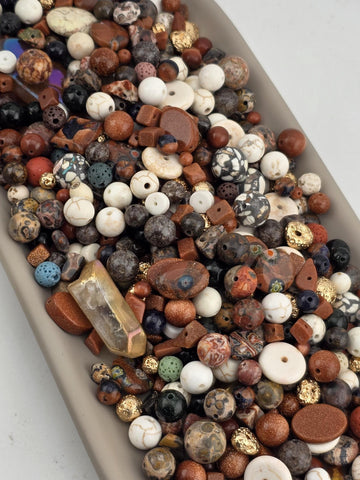 A collection of various beads, gemstones, and crystals of different shapes, sizes, and colors, including white, brown, black, and multicolored stones, arranged in a visually appealing manner.