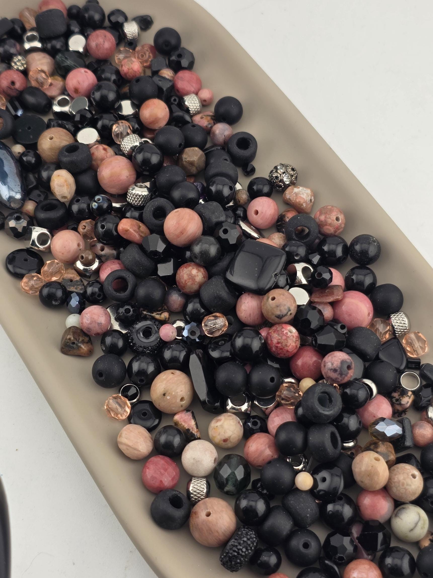 A collection of various beads, including black, pink, and multicolored beads, are scattered on a surface.