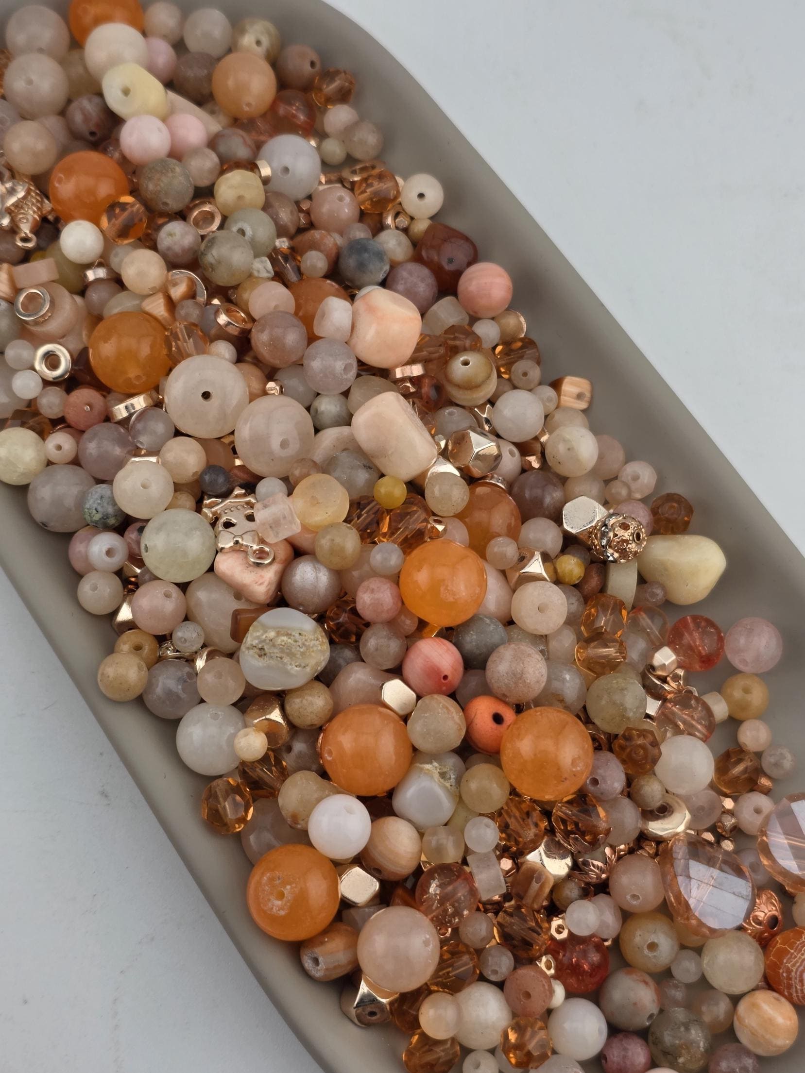 A collection of various beads and beads in different shapes, sizes, and colors, including gold, orange, and white, arranged in a bowl or container.