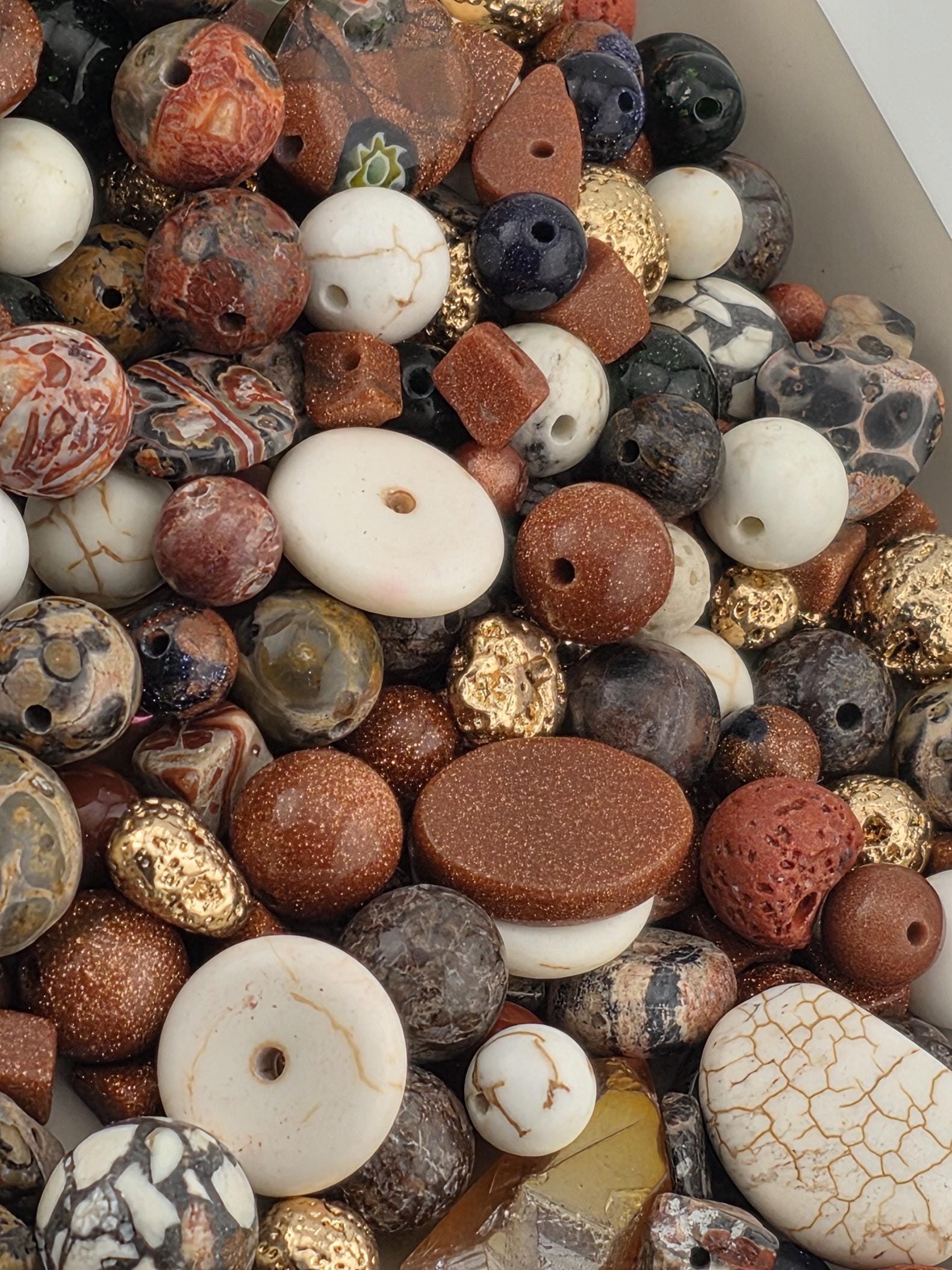 The image is a close-up of a pile of various beads, including white, brown, and multicolored beads, as well as some larger stones.