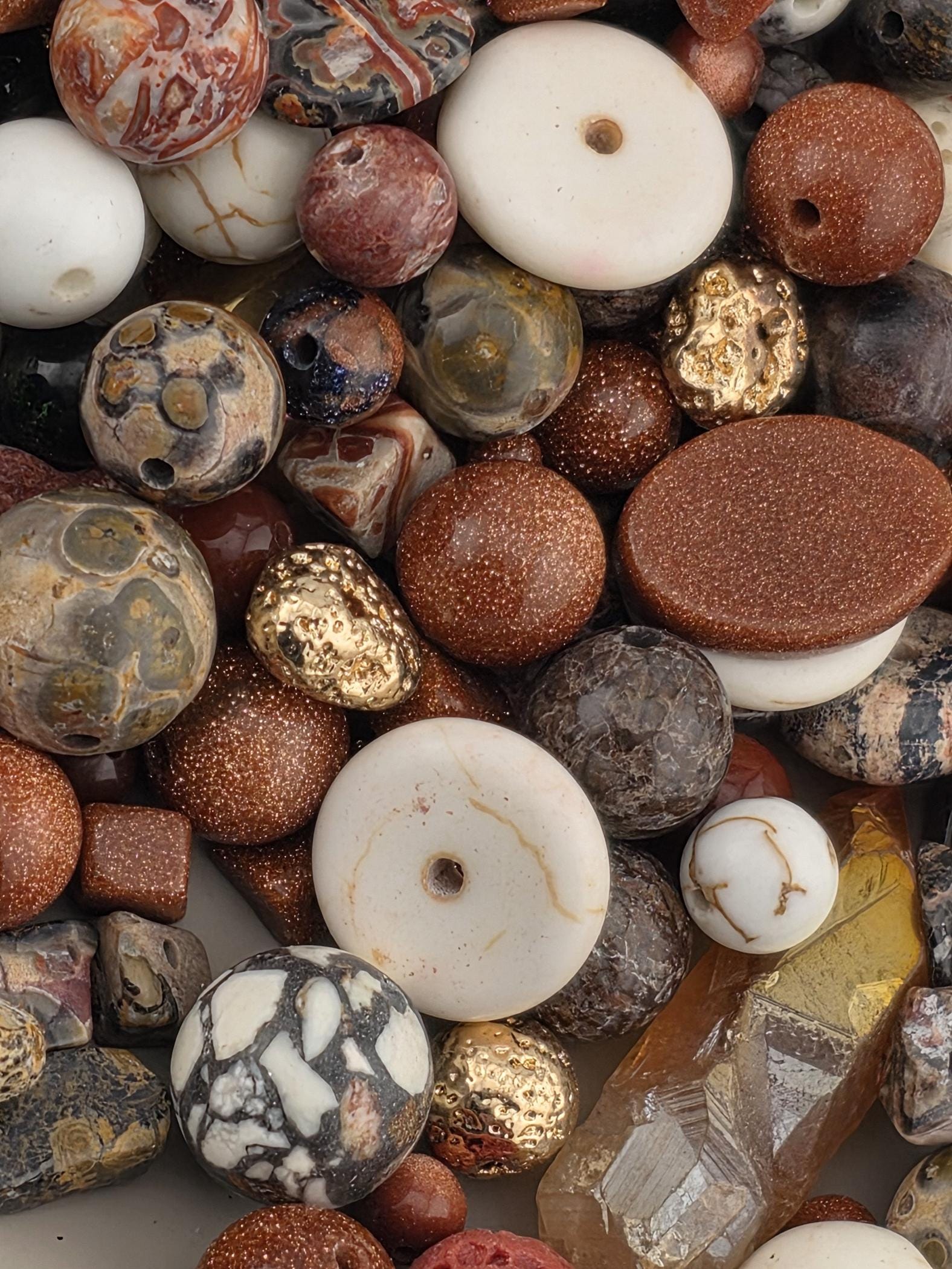 The image is a close-up of various beads and stones, including white, brown, and multicolored beads, as well as some larger stones.