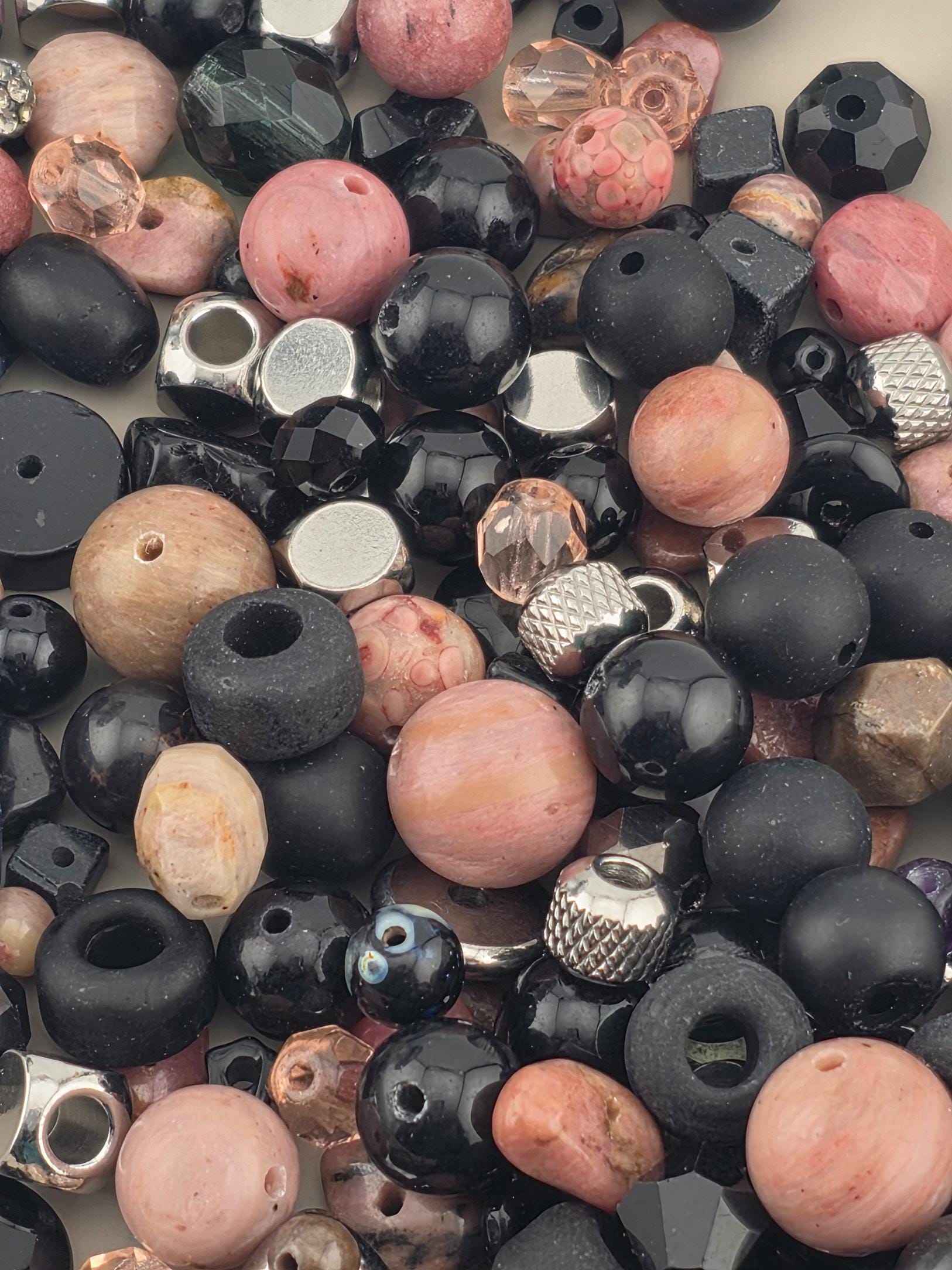 The image is a collection of various beads and beads in different shapes, sizes, and colors, including black, pink, and silver beads.