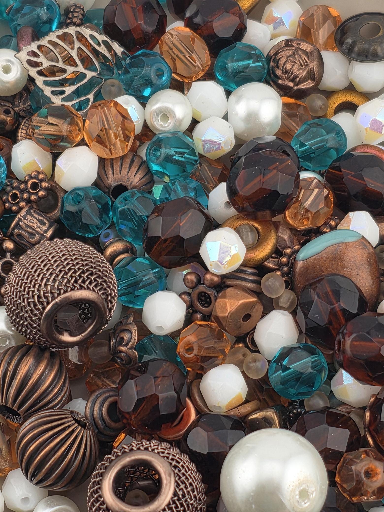 The image is a close-up of various beads and beads, including white, blue, brown, and copper-colored beads, as well as some metal beads.