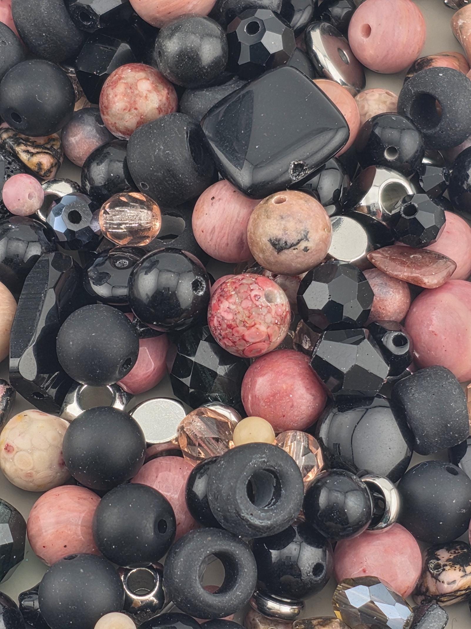 The image is a close-up of various beads and beads, including black, pink, and silver beads, scattered together.