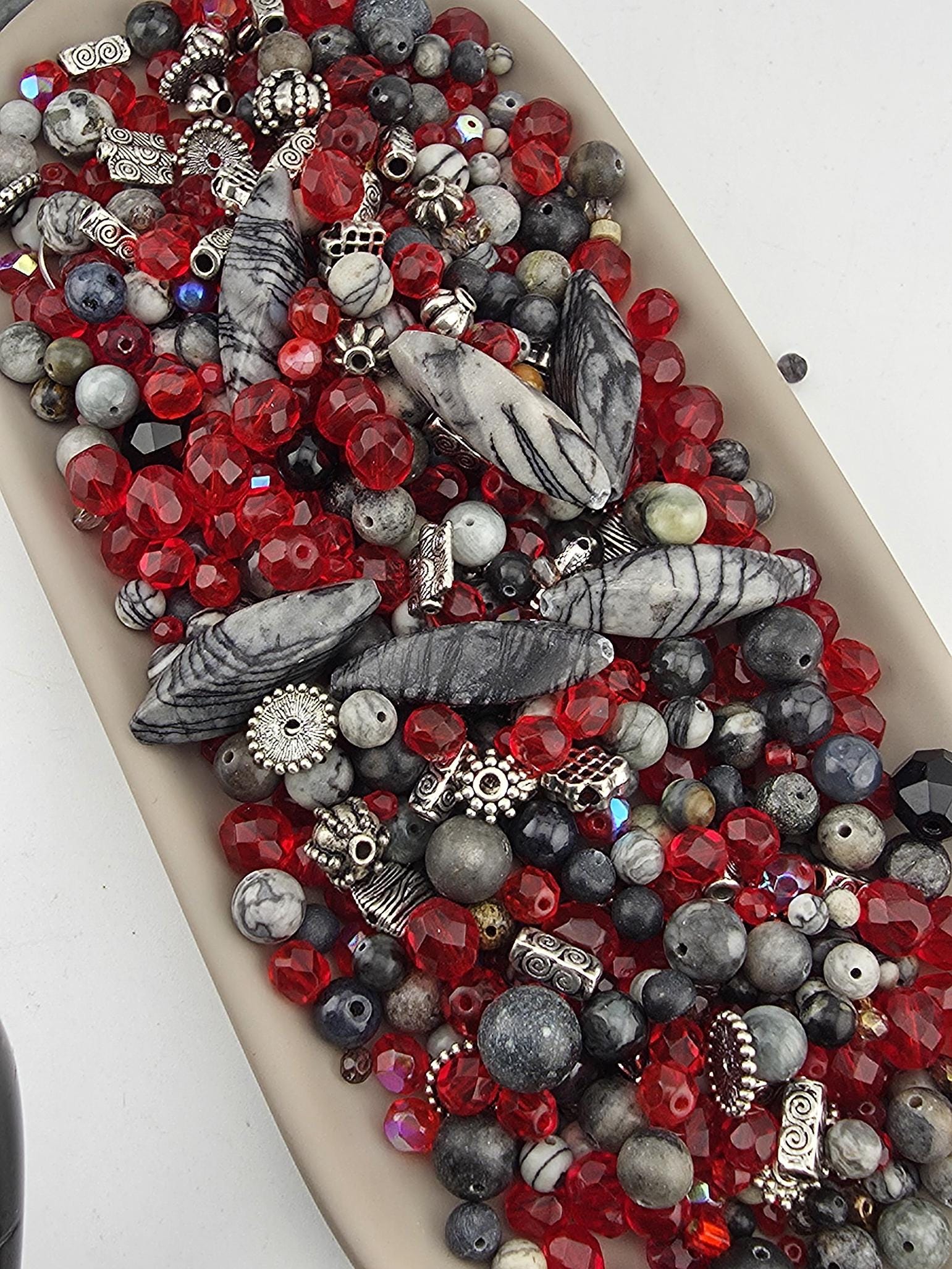 A collection of various beads, including red, black, and gray beads, as well as some silver and black beads, arranged on a surface.