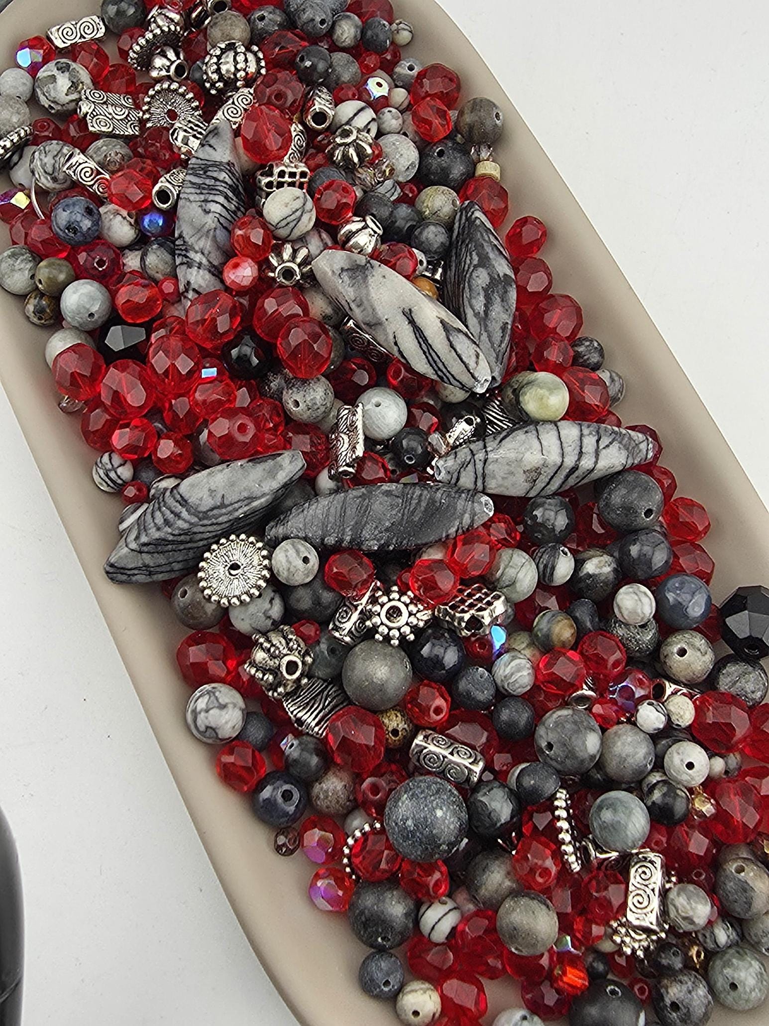 A collection of various beads, including red, black, and gray beads, as well as some silver and white beads, arranged on a surface.