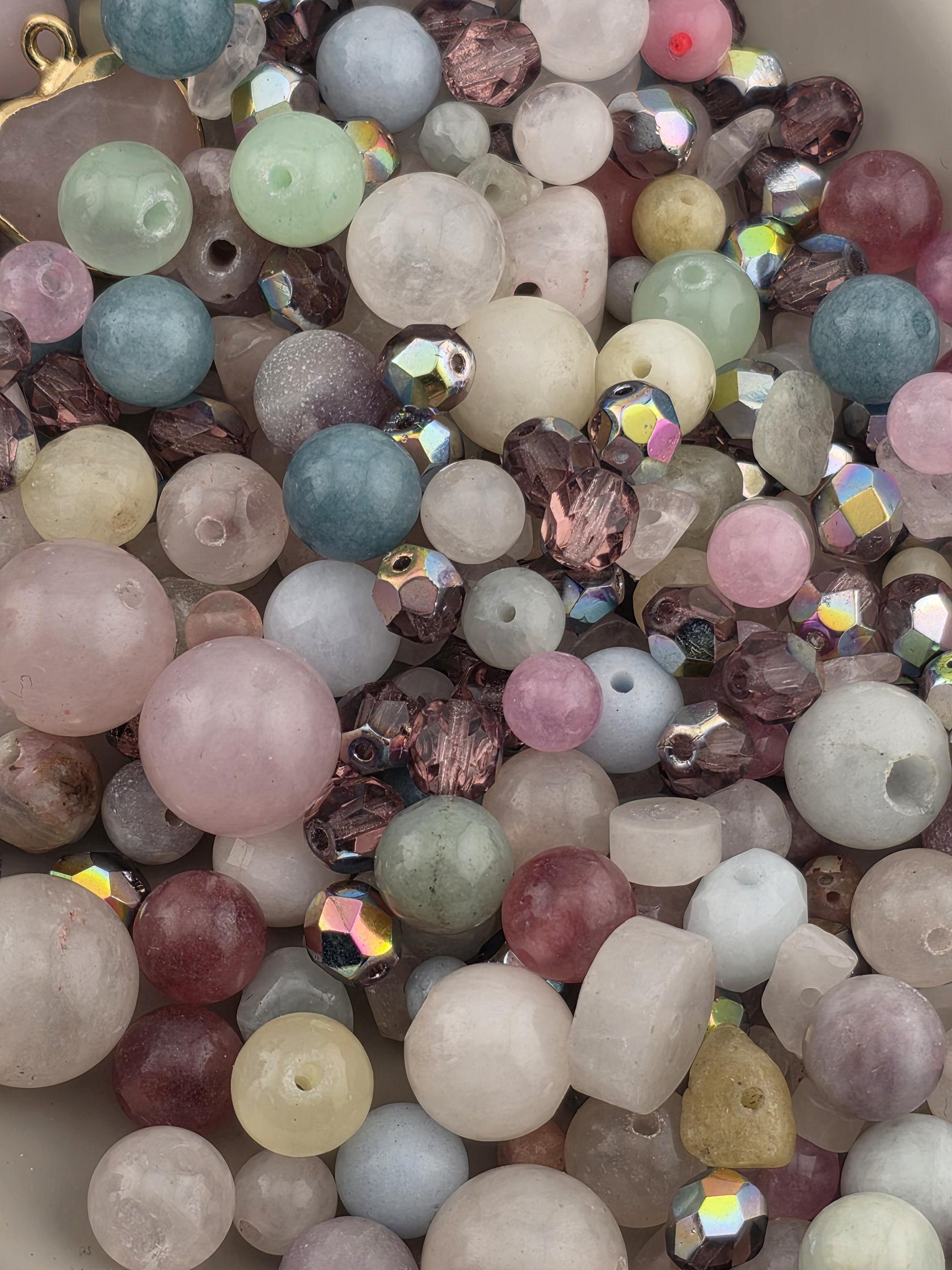 A close-up image of a variety of colorful beads and crystals, including clear, pink, purple, and multicolored stones, scattered together.