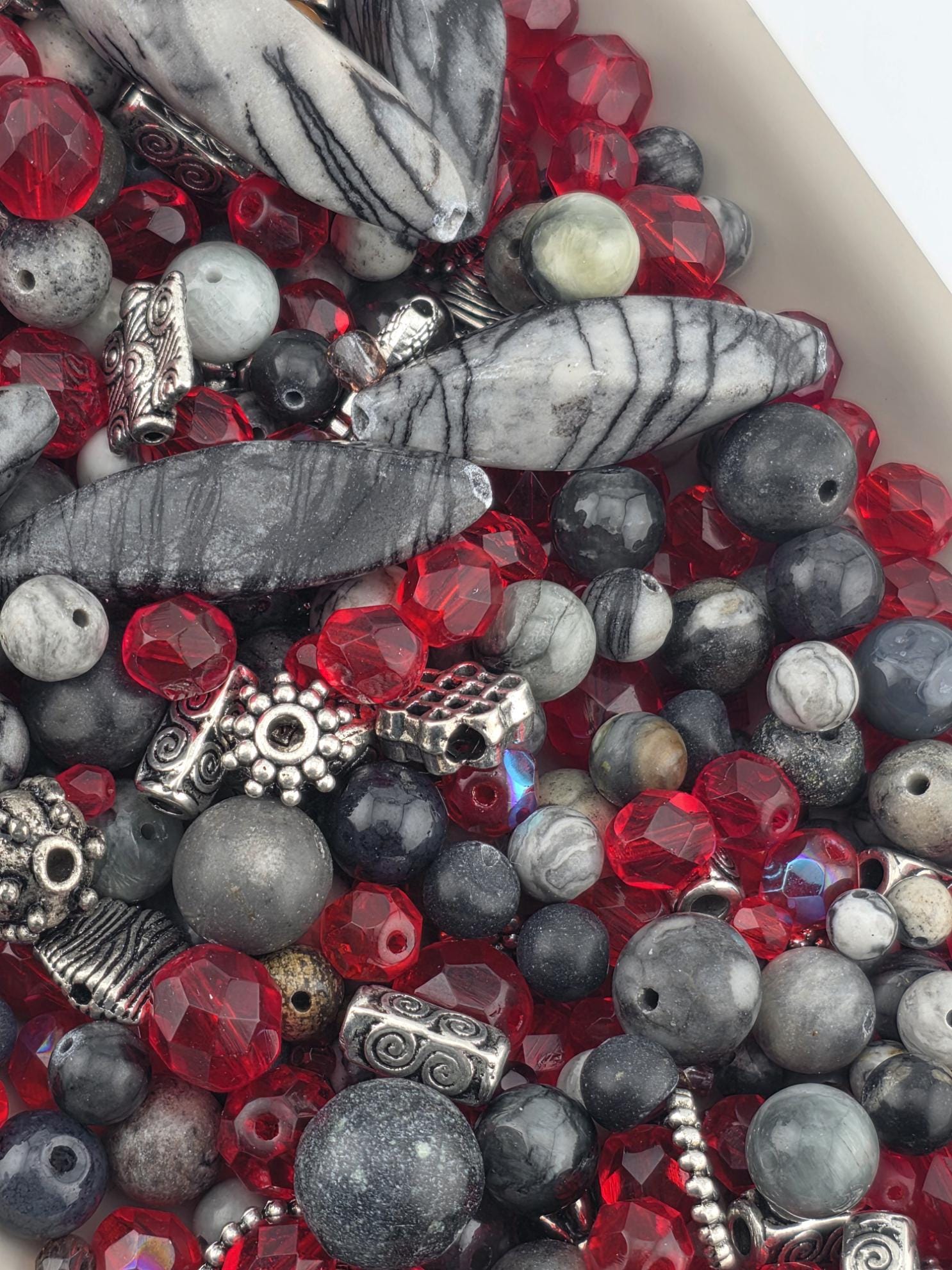 a collection of various beads and stones, including red, gray, and black beads, as well as some metallic elements.
