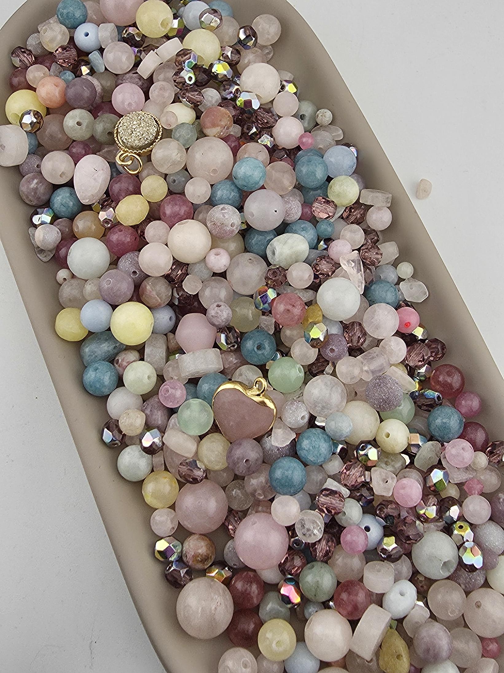 A large collection of colorful beads and gemstones arranged in a tray or bowl, with various shapes and sizes.