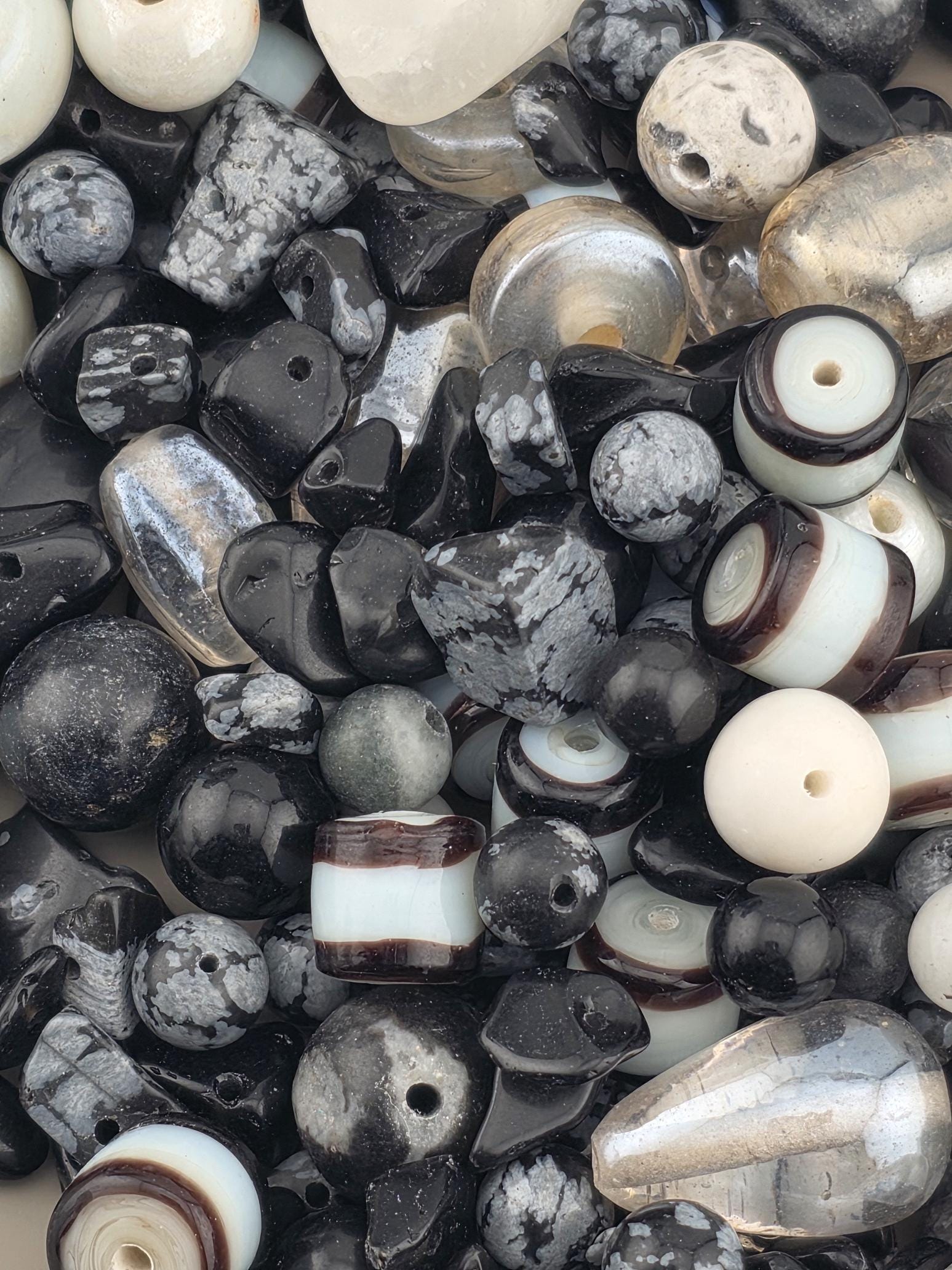 The image is a close-up of various beads and stones, including black, white, and silver-colored beads, as well as some larger stones.
