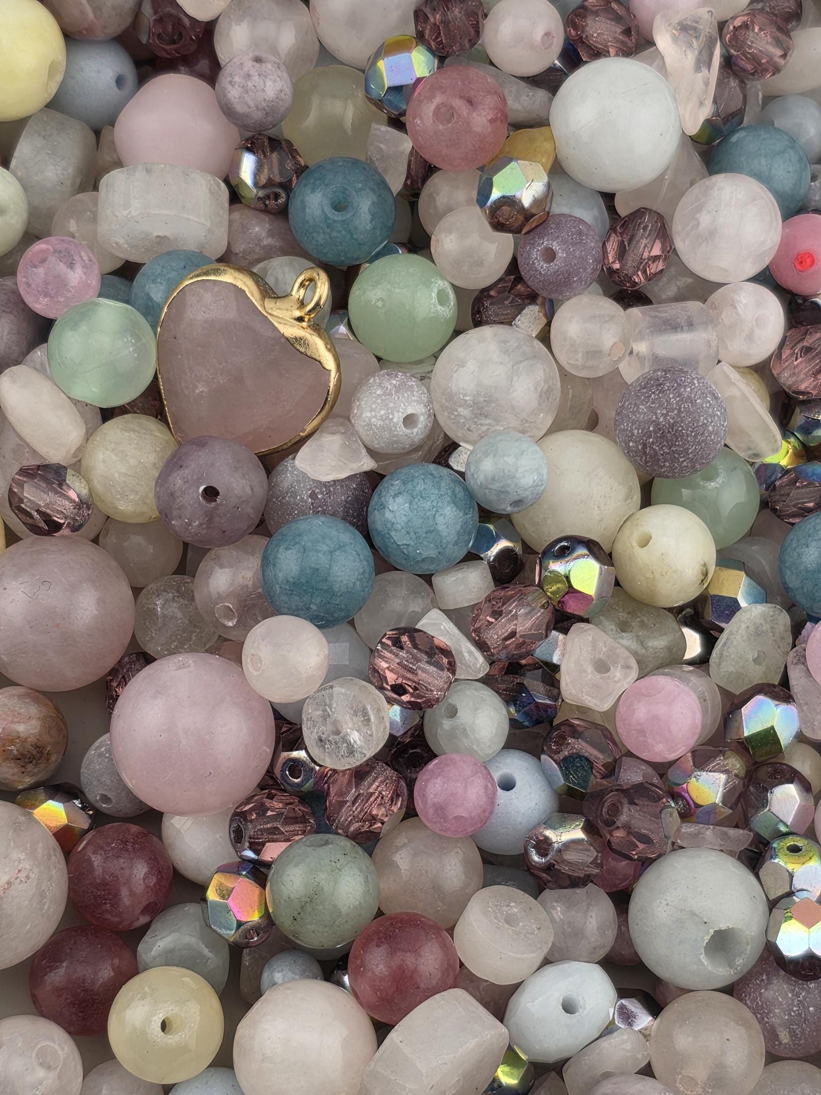 The image is a close-up of a collection of various colored beads, including clear, white, and multicolored beads, as well as a gold-colored pendant.