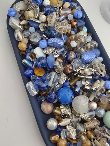 A collection of various colorful beads, including blue, silver, and multicolored glass beads, arranged on a dark surface.