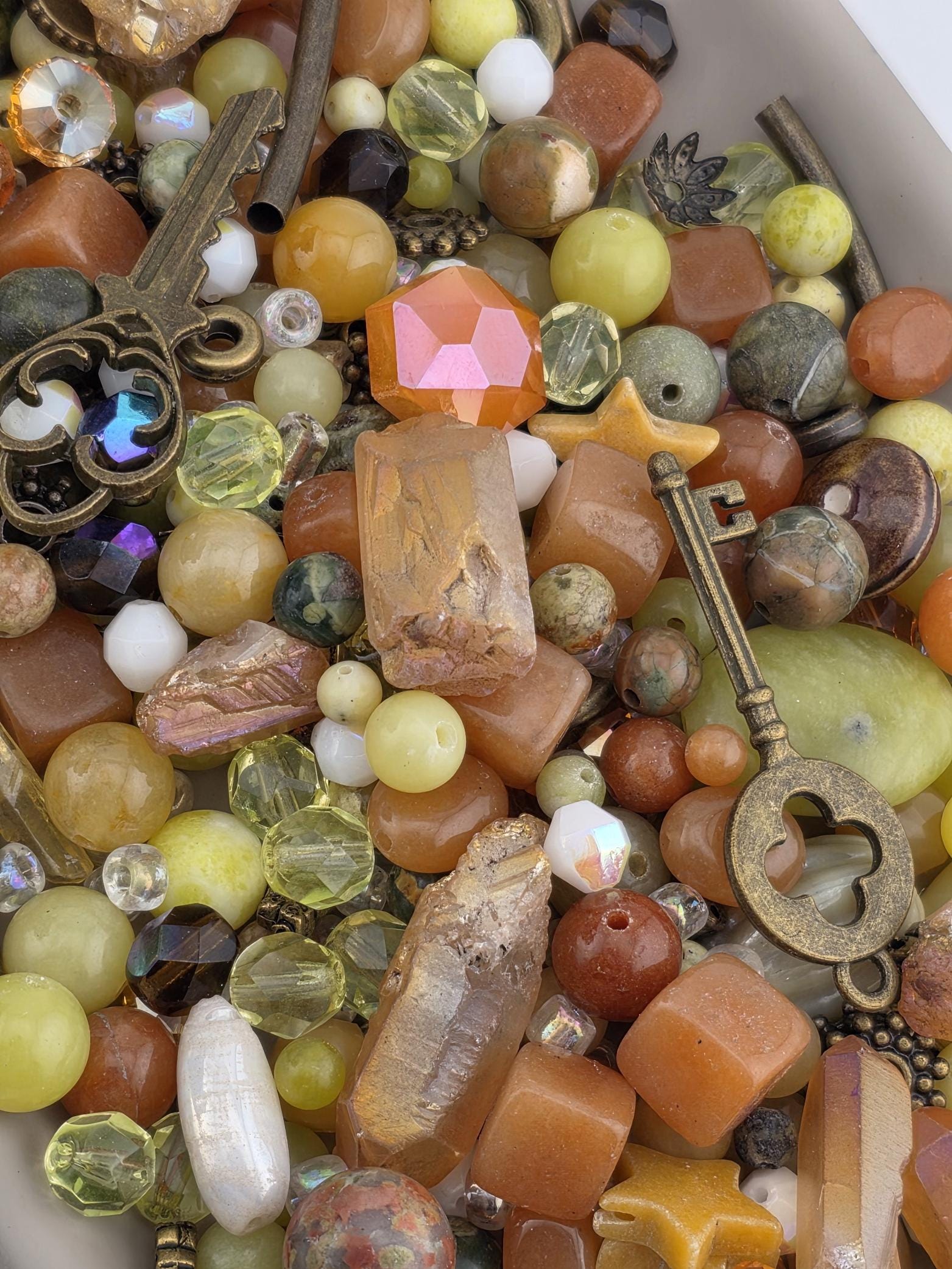 The image is a close-up of a collection of various beads, gemstones, and metal objects, including a key, arranged in a visually appealing manner.