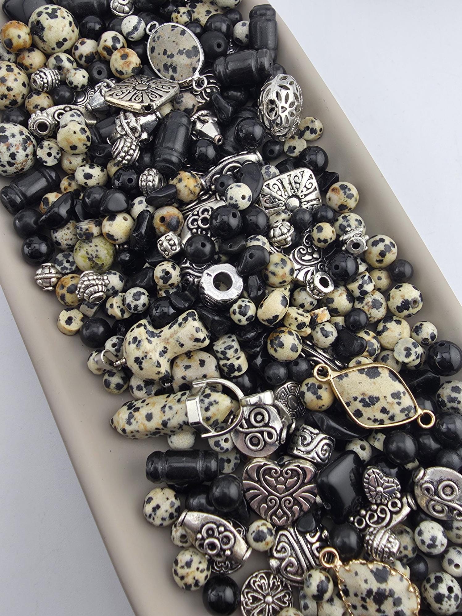 A collection of various beads, charms, and metal pieces in shades of black, white, and gold, arranged on a surface.