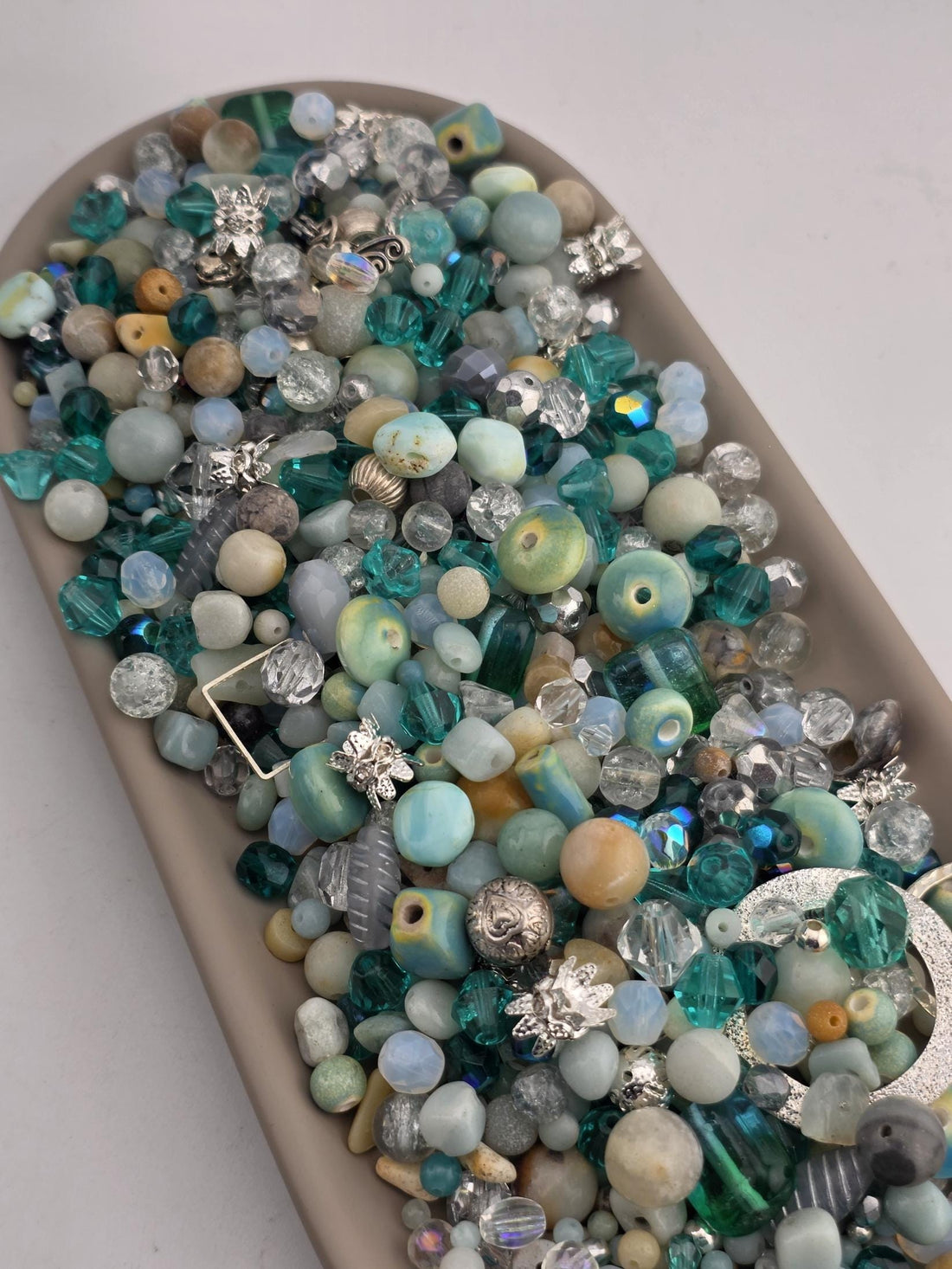 A collection of various colorful beads, including blue, green, and silver, arranged in a tray or container.