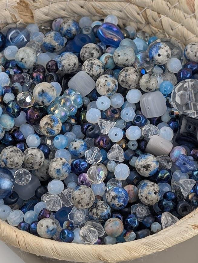 A woven basket filled with a variety of colorful beads, including clear, blue, and multicolored glass beads.