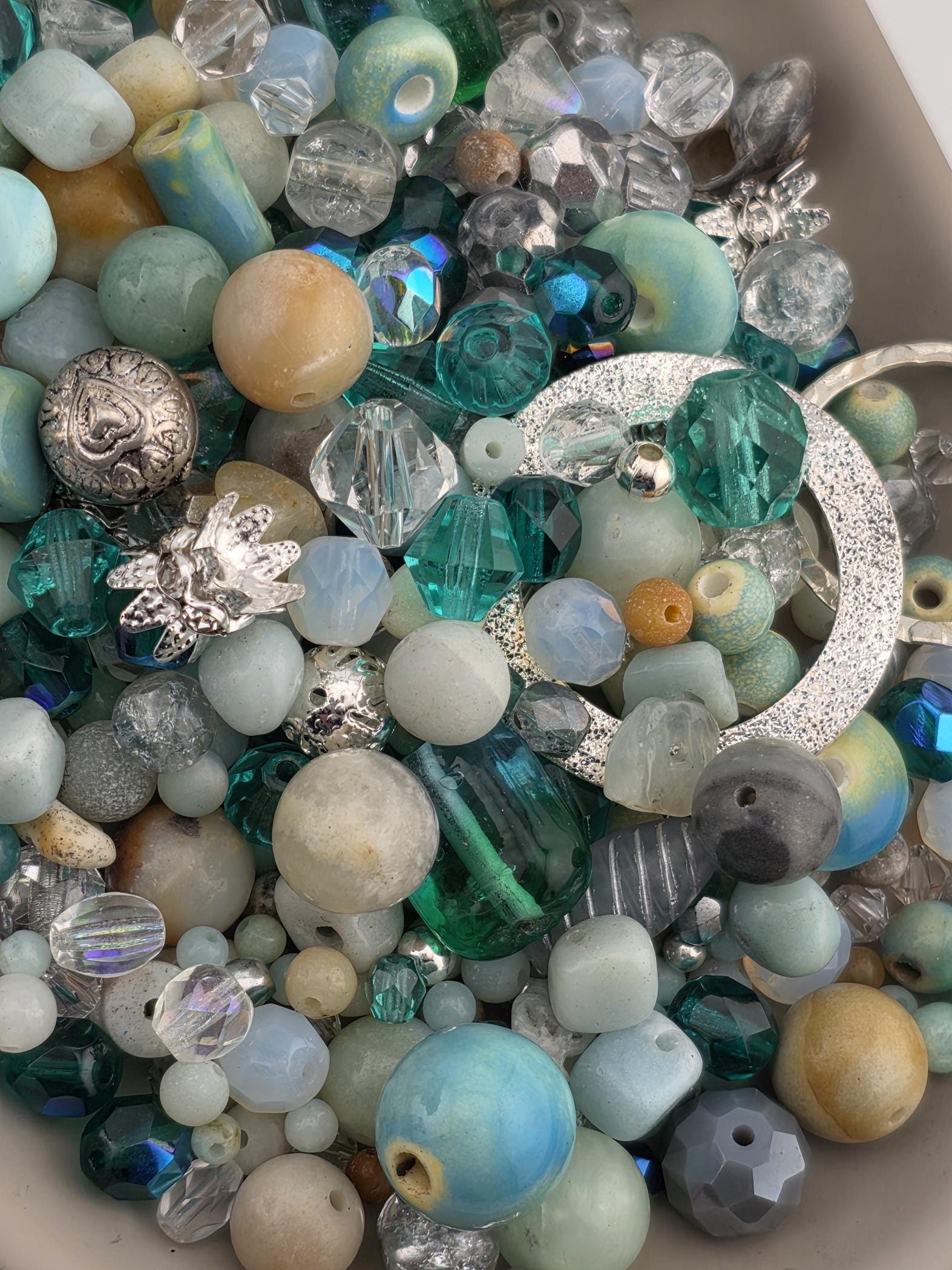A close-up image of a variety of colorful beads and beads, including clear, blue, green, and silver beads, as well as some with intricate designs.
