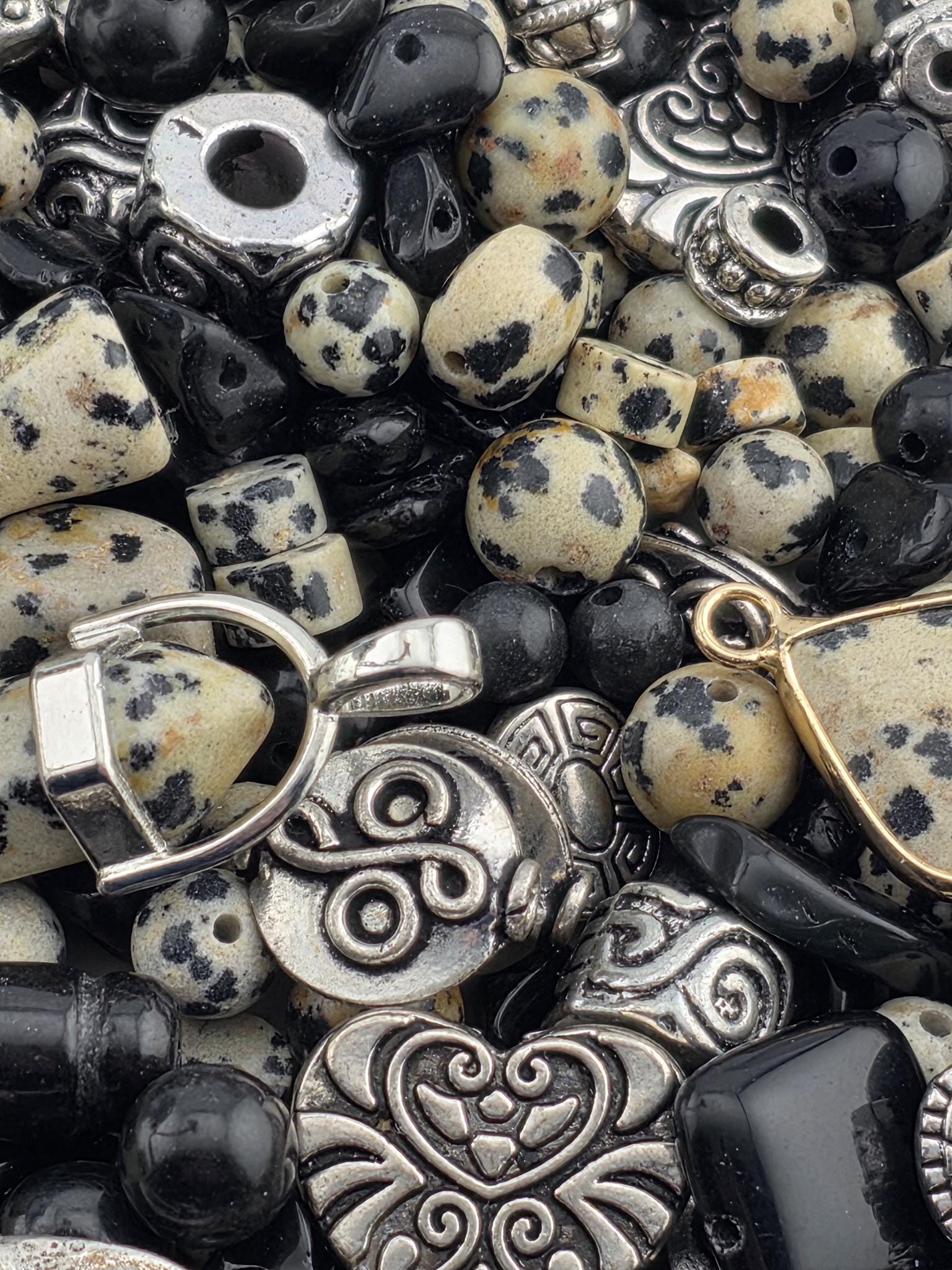 The image is a close-up of various beads, charms, and pendants in shades of black and white, including beads, charms, and pendants.