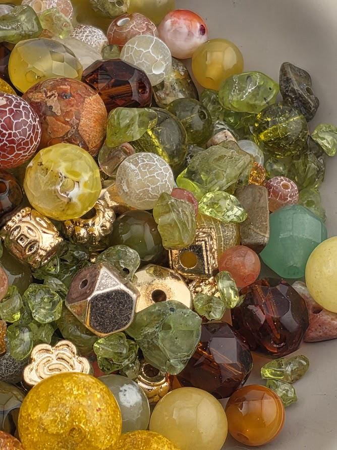 The image is a close-up of a pile of various colorful beads, including glass, metal, and gemstone beads, scattered together.