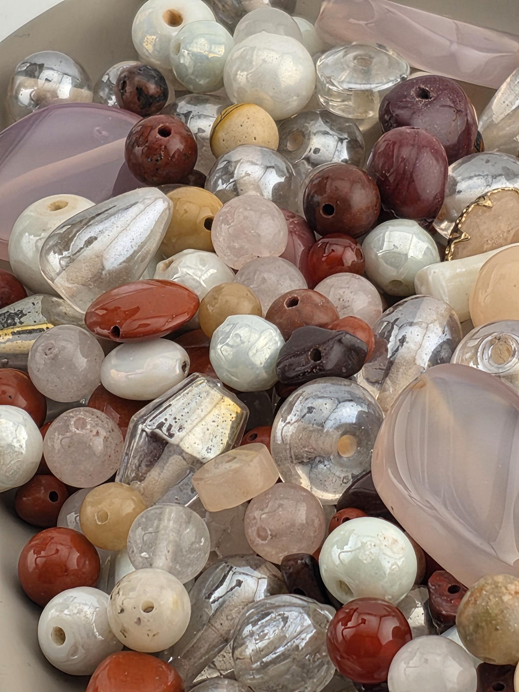 A close-up image of various colorful beads and stones, including clear, brown, and multicolored beads, arranged in a pile.
