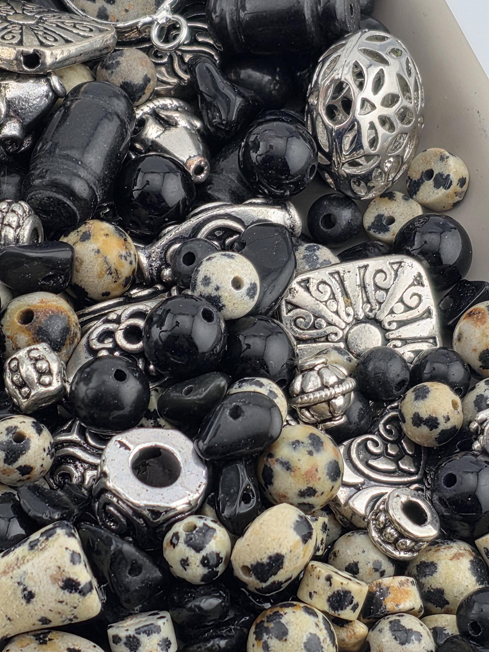 a variety of beads and metal pieces, including black and white beads, silver and black beads, and some with intricate designs.