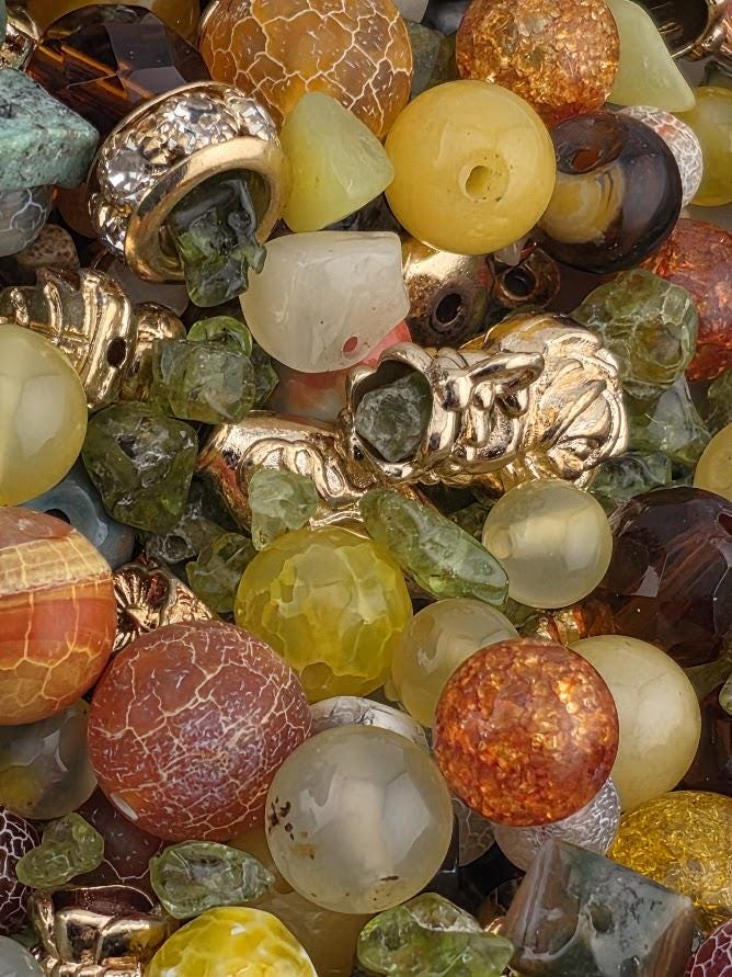 The image is a close-up of a collection of various colorful beads, gemstones, and metal pieces, creating a visually appealing and diverse assortment of materials.