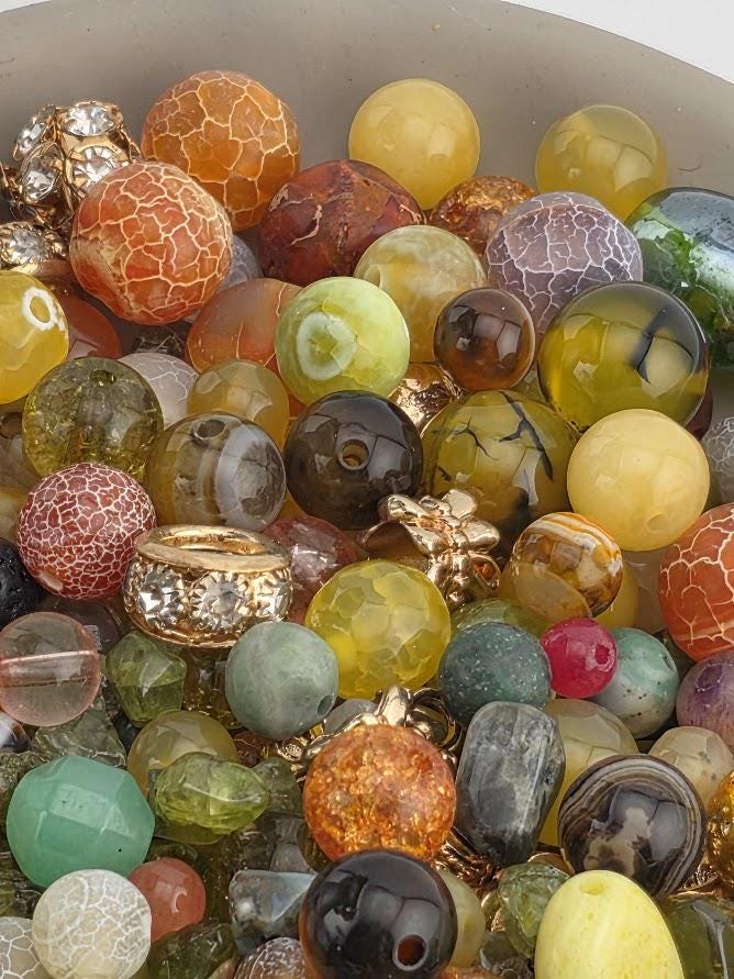 The image is a collection of various colorful beads and gemstones, including multicolored glass beads, gemstone beads, and other decorative elements.