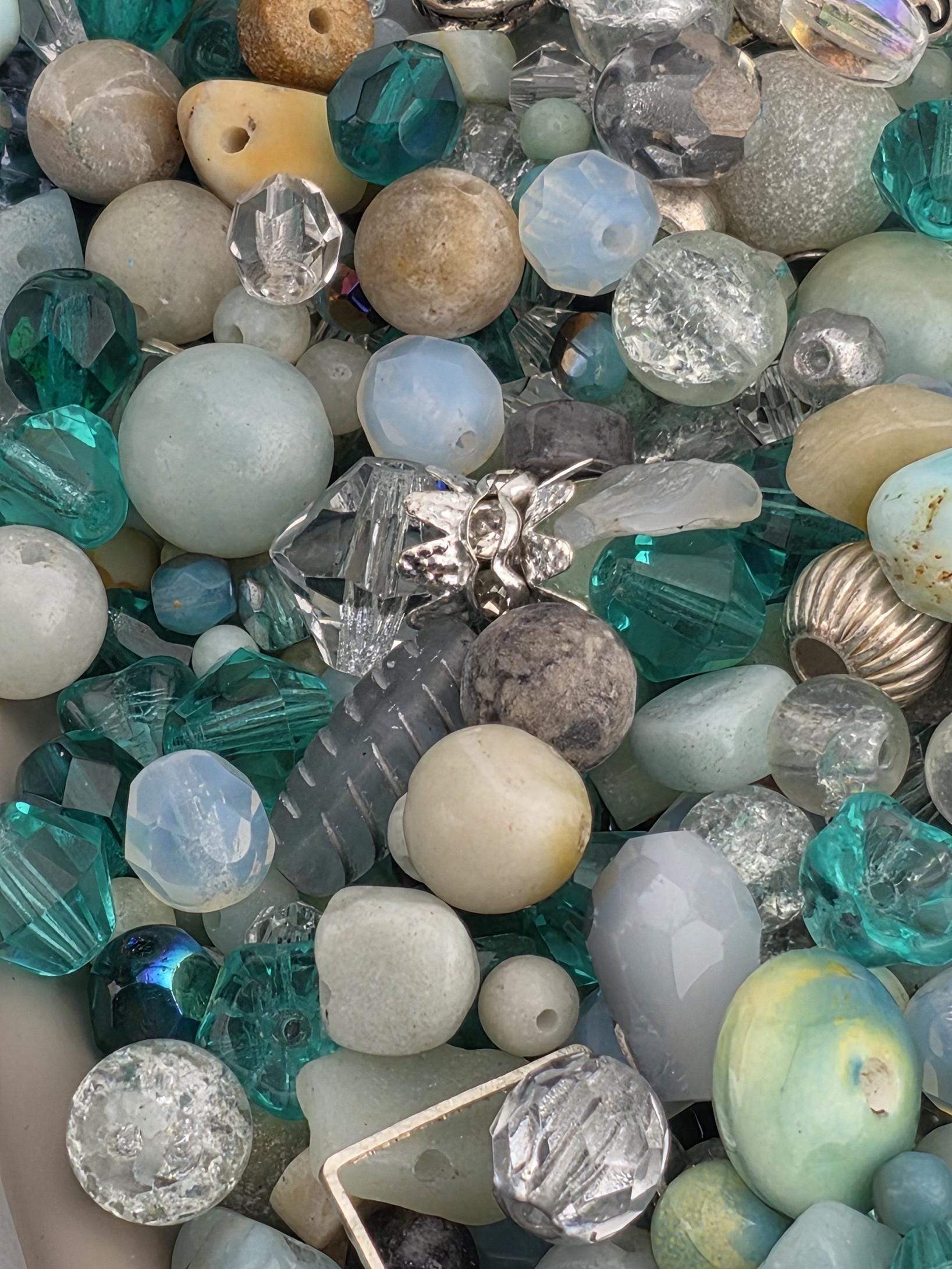 The image is a close-up of various colorful beads and gemstones, including turquoise, white, and silver beads, as well as some larger stones.