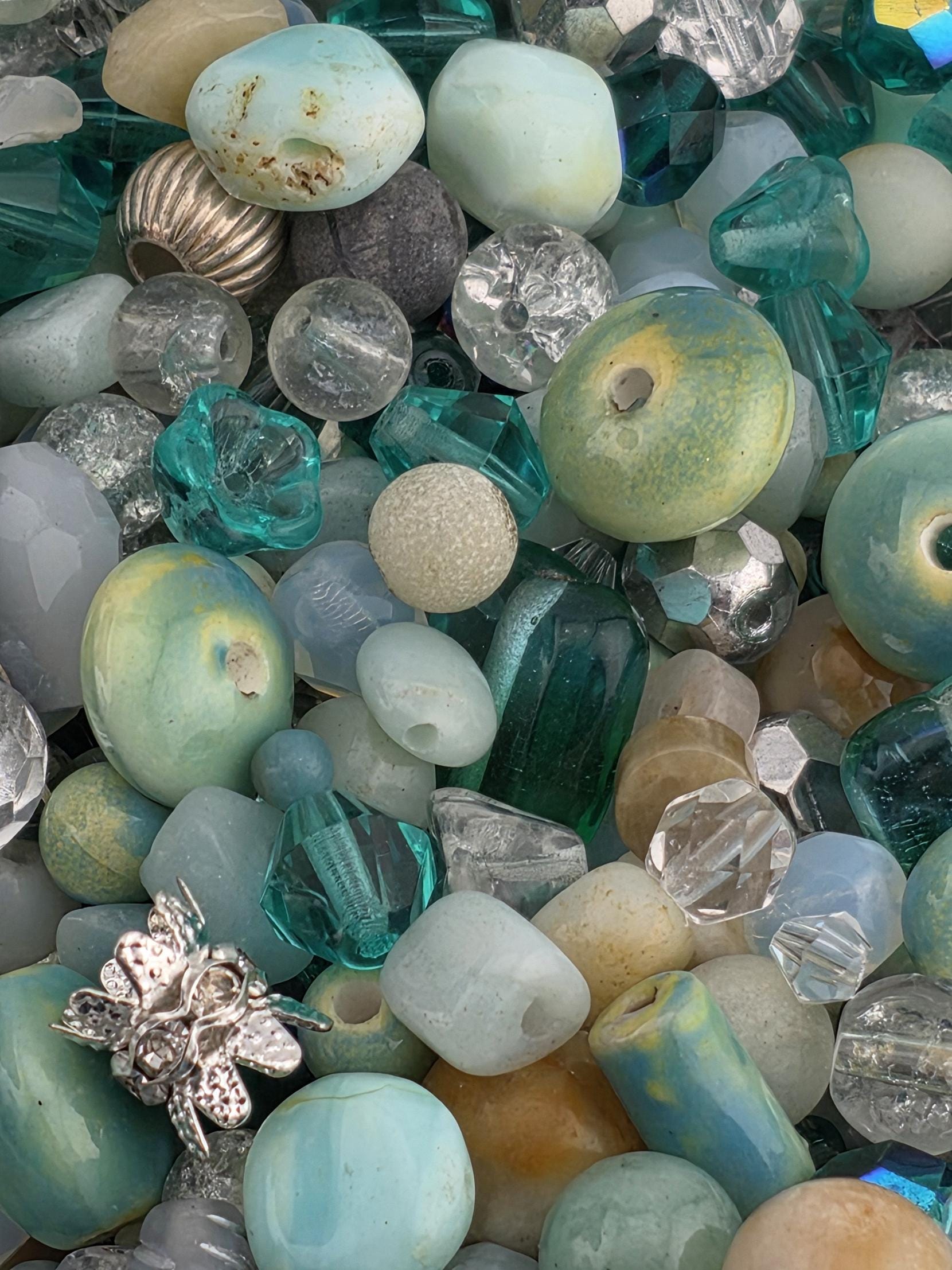 The image is a close-up of various beads and glass objects, including clear, blue, green, and silver beads, as well as some glass beads and other glass objects.
