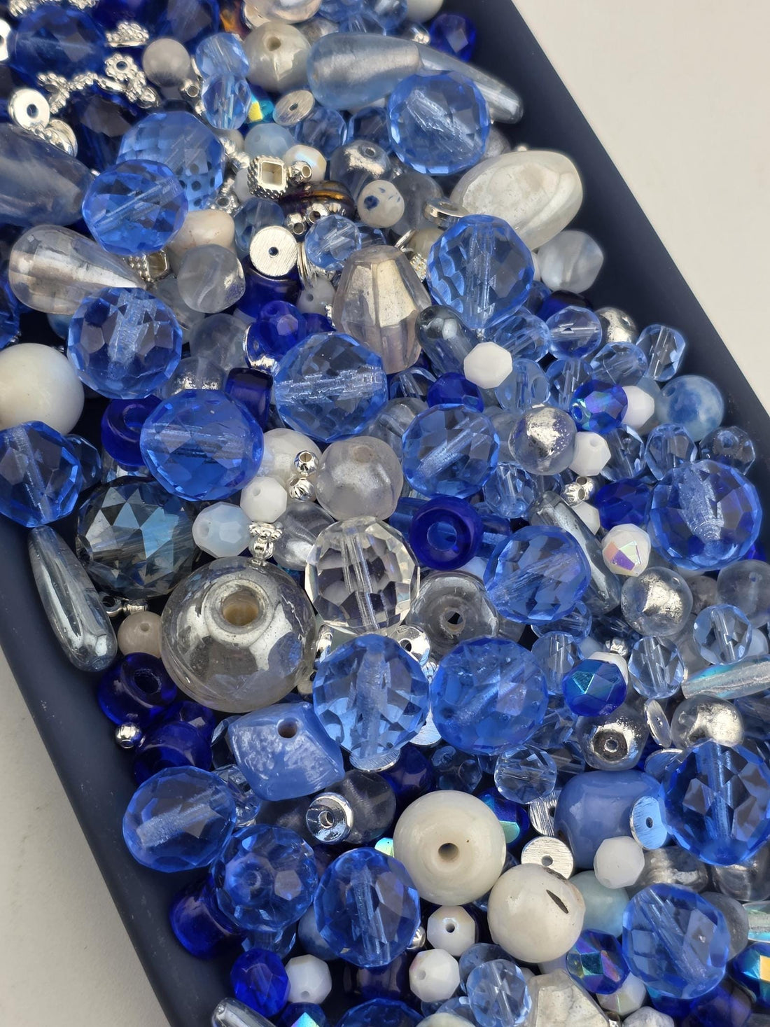 A collection of various blue and silver glass beads, including clear, blue, and silver beads, arranged in a visually appealing manner.