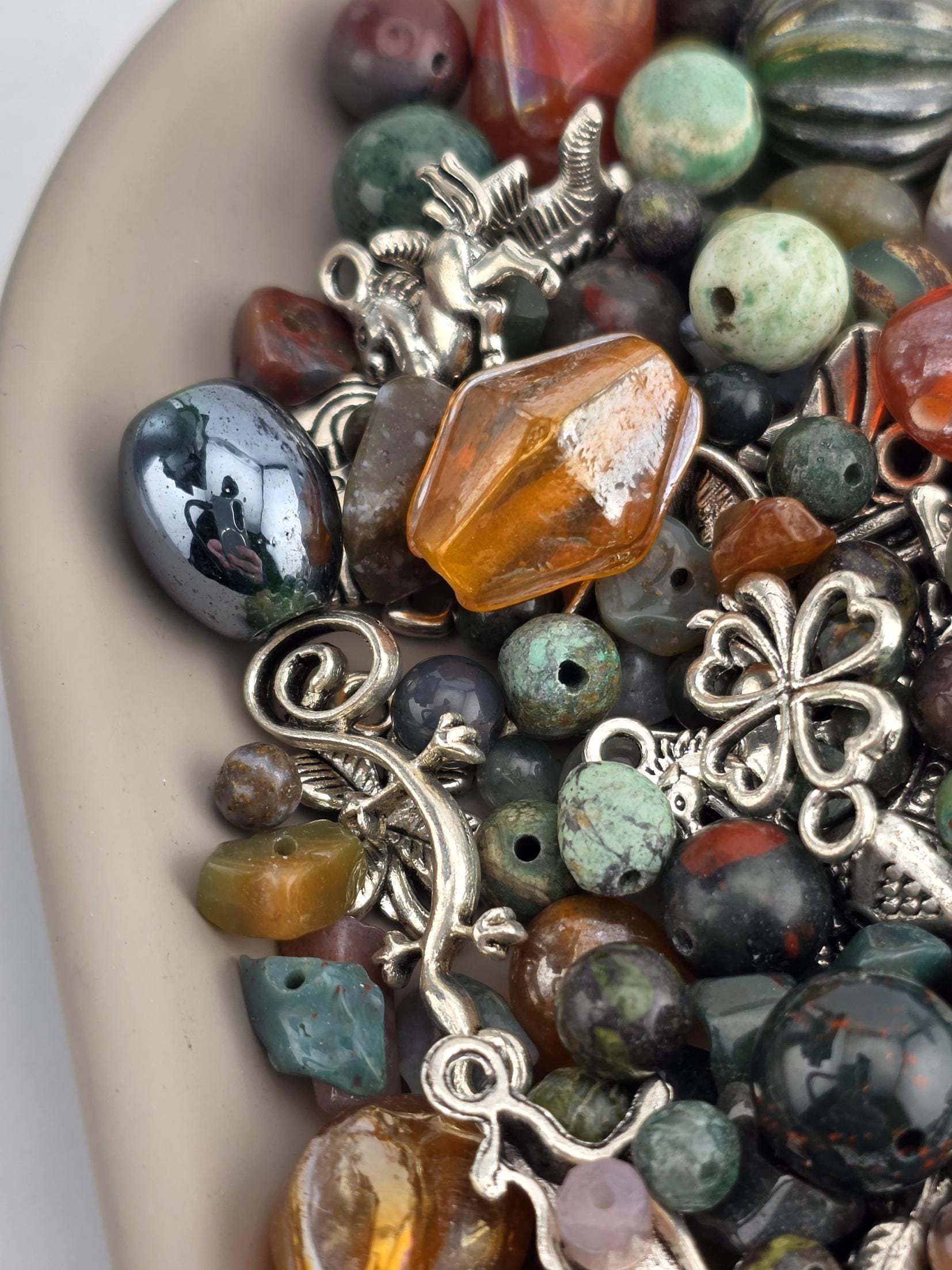 The image is a close-up of a collection of various beads, charms, and metal pieces, including gemstones and beads in different colors and shapes.