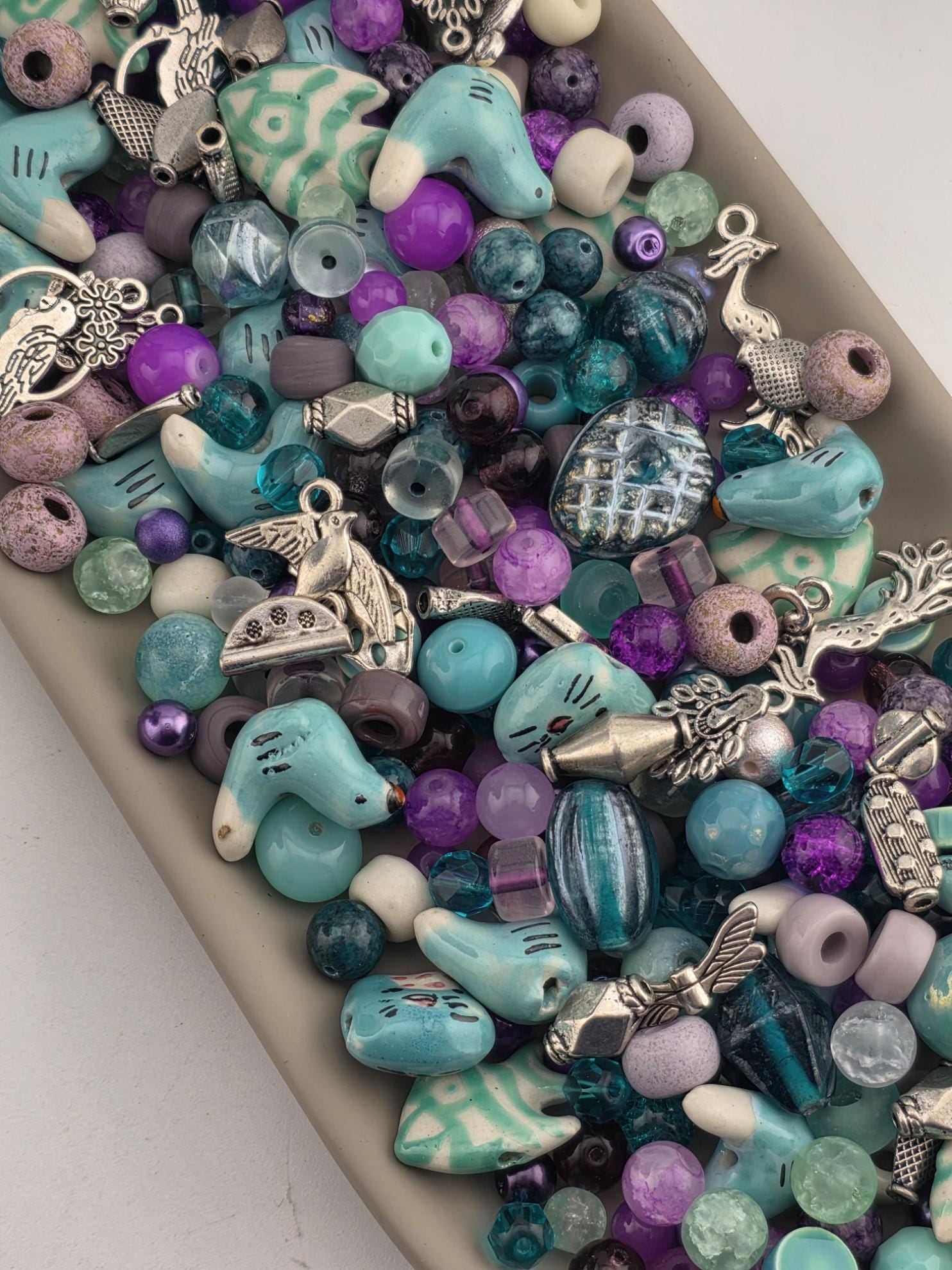 A collection of various colorful beads, charms, and trinkets in shades of blue, purple, and green, arranged in a visually appealing manner.